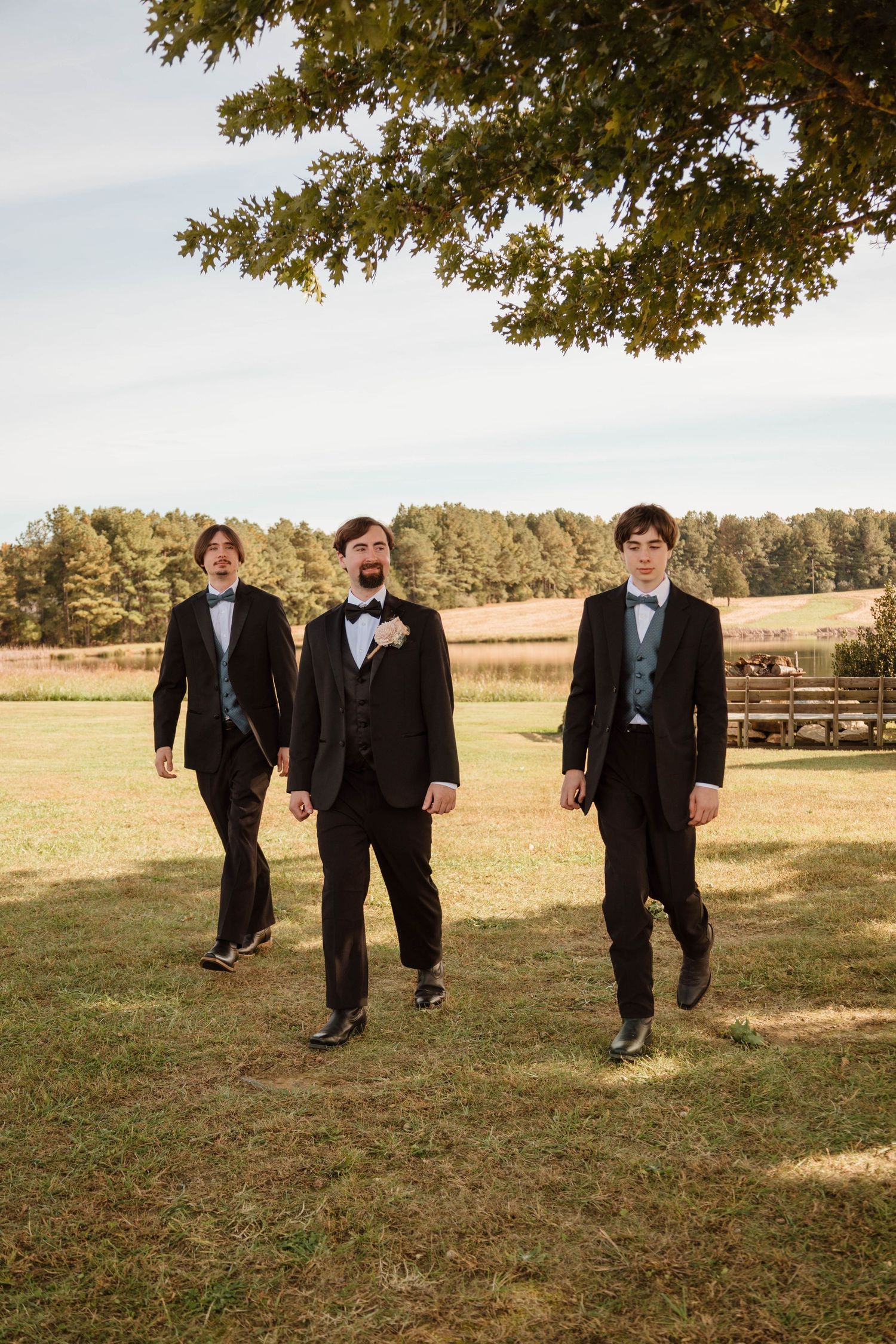 Groomsmen in black suits walking across a grassy field.