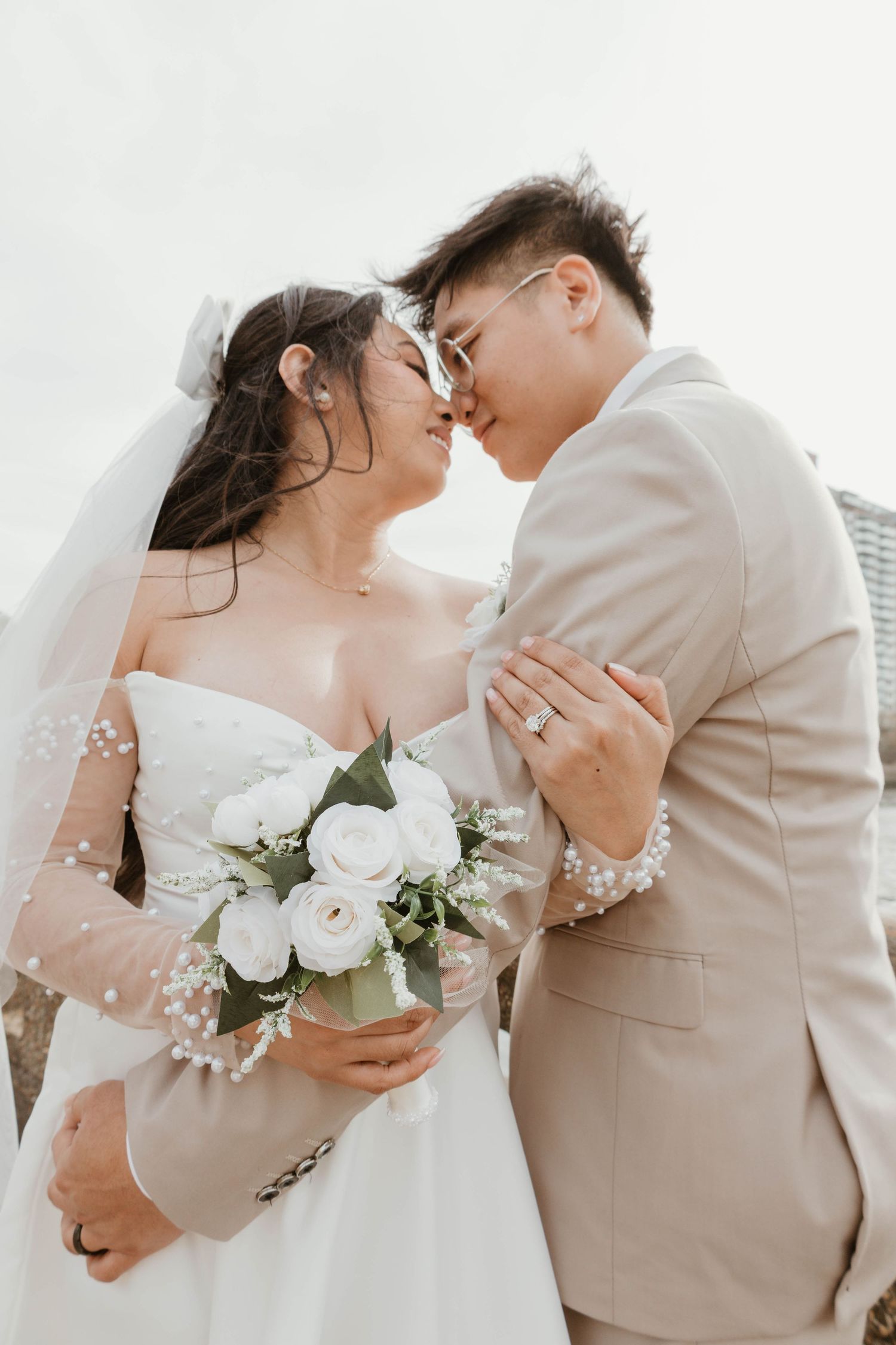 A bride and groom embrace tenderly on their wedding day, with the bride holding a bouquet of white roses.