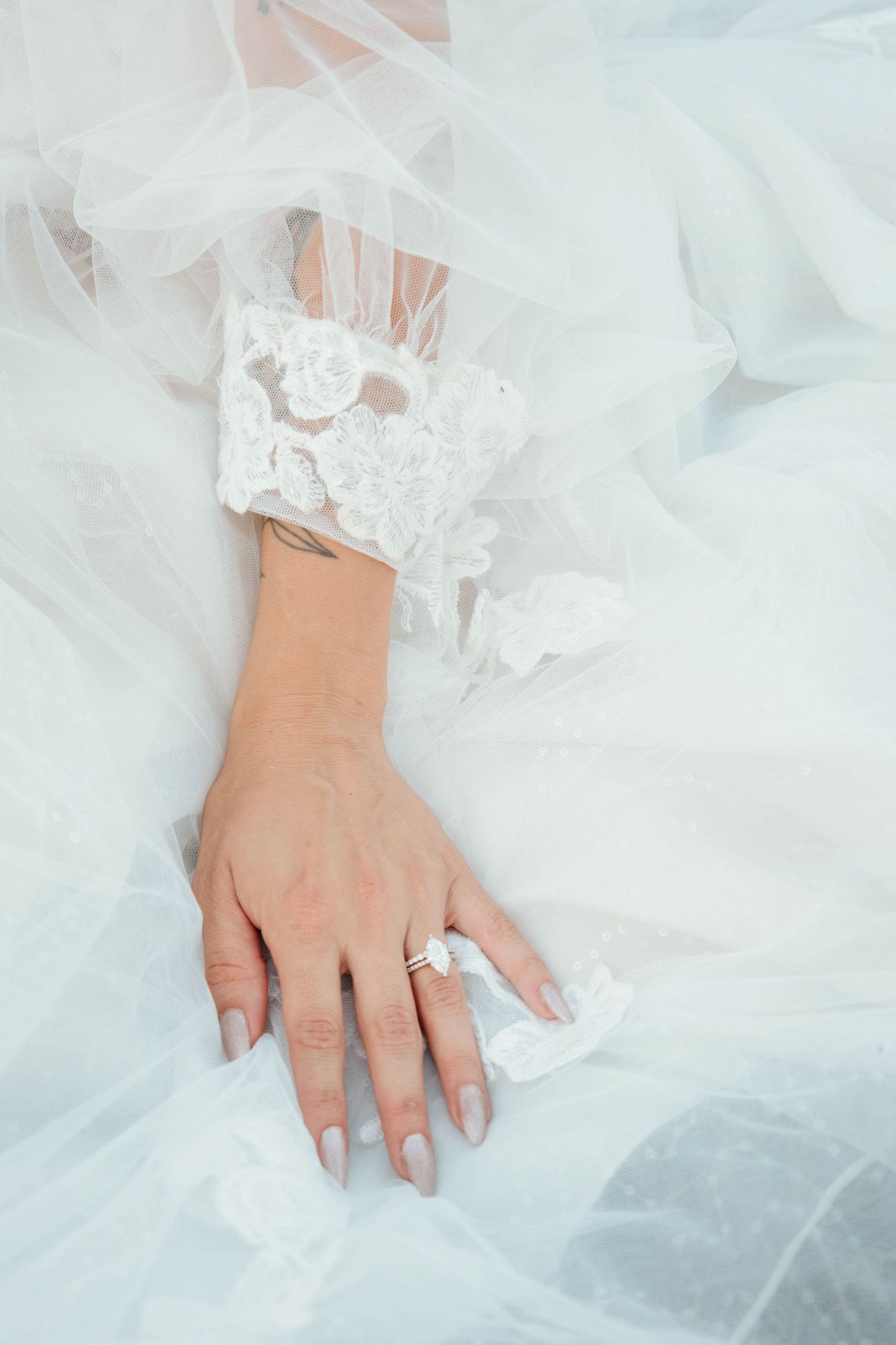 Close-up shots of hands adorned in wedding attire against flowing white tulle fabric.
