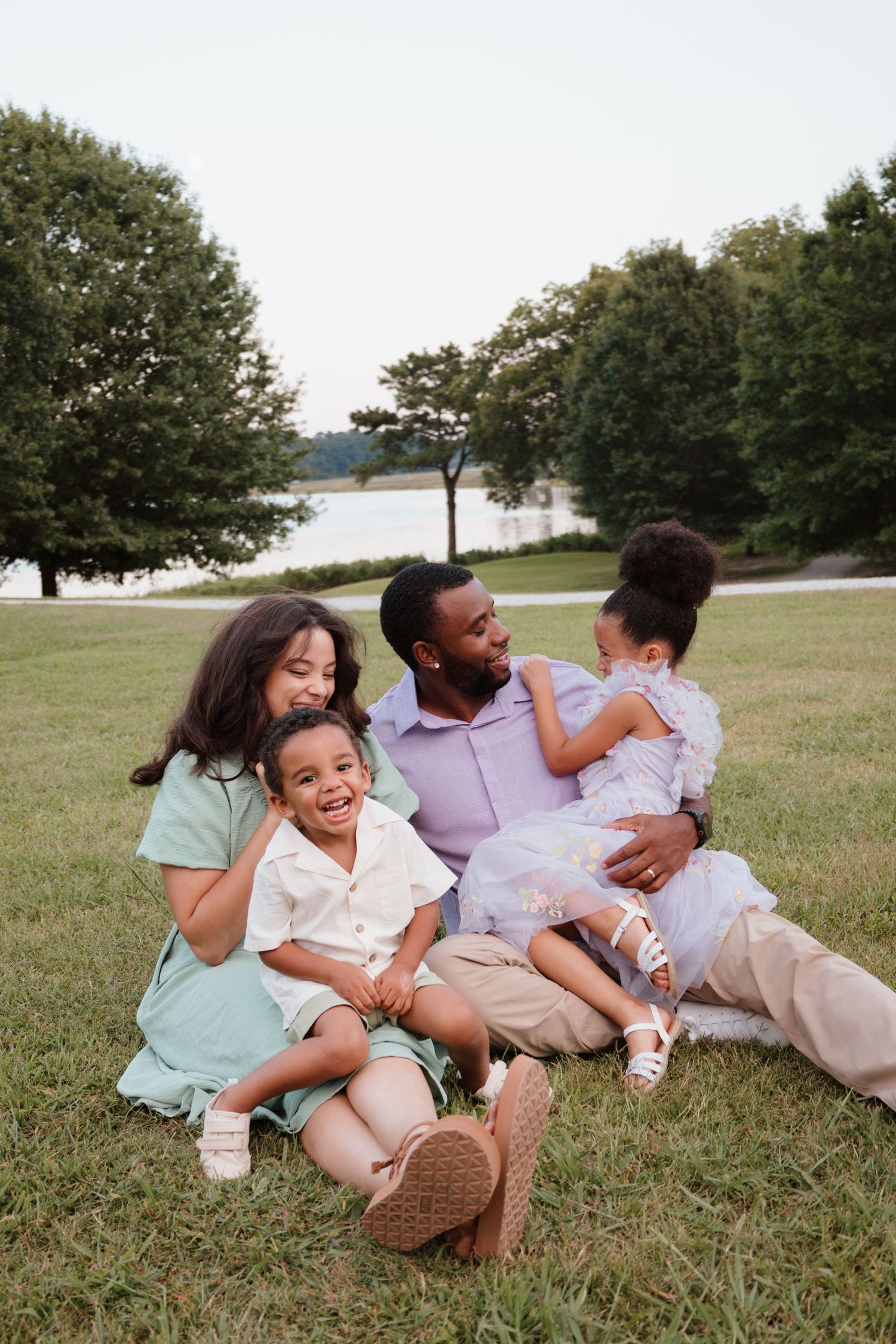 Family relaxing together on grassy field during outdoor photoshoot in casual attire.