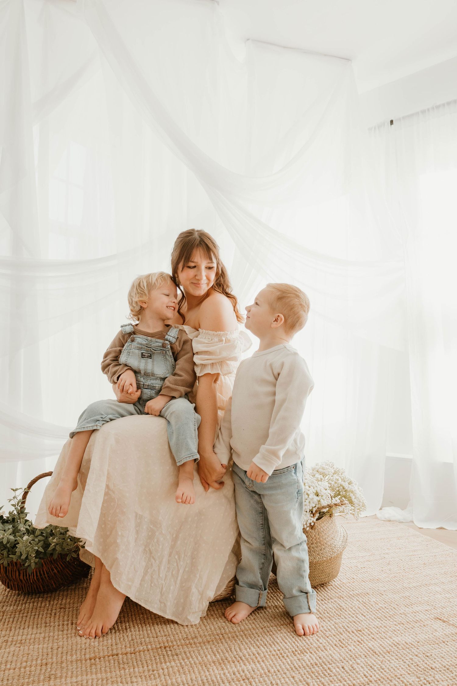 A soft and bright family portrait in white room with natural light, jute rug and woven basket with dried flowers.