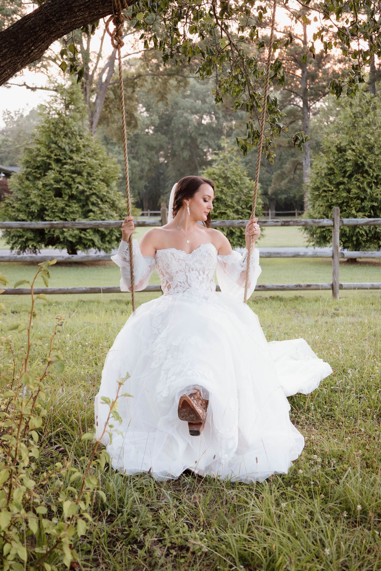 A bride in a white ballgown sits on a wooden swing in a garden setting.