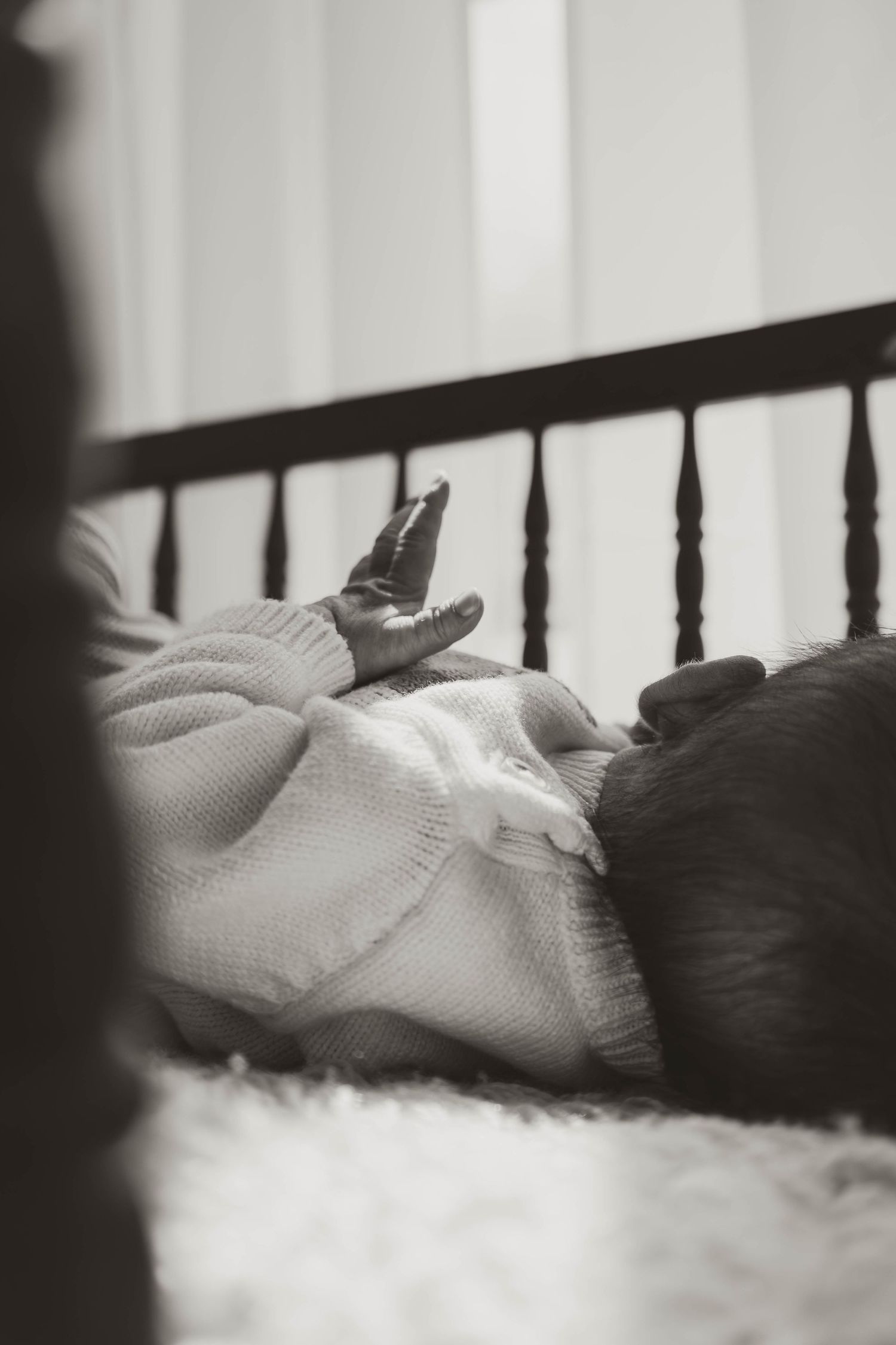 Black and white photo of a sleeping newborn baby lying in a crib, wrapped in a soft knit blanket.