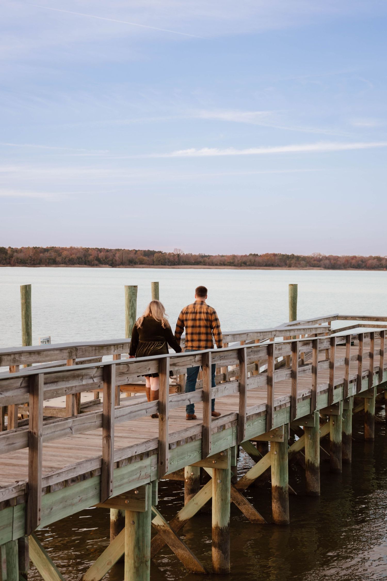Couple walking on wooden pier overlooking calm lake during autumn.