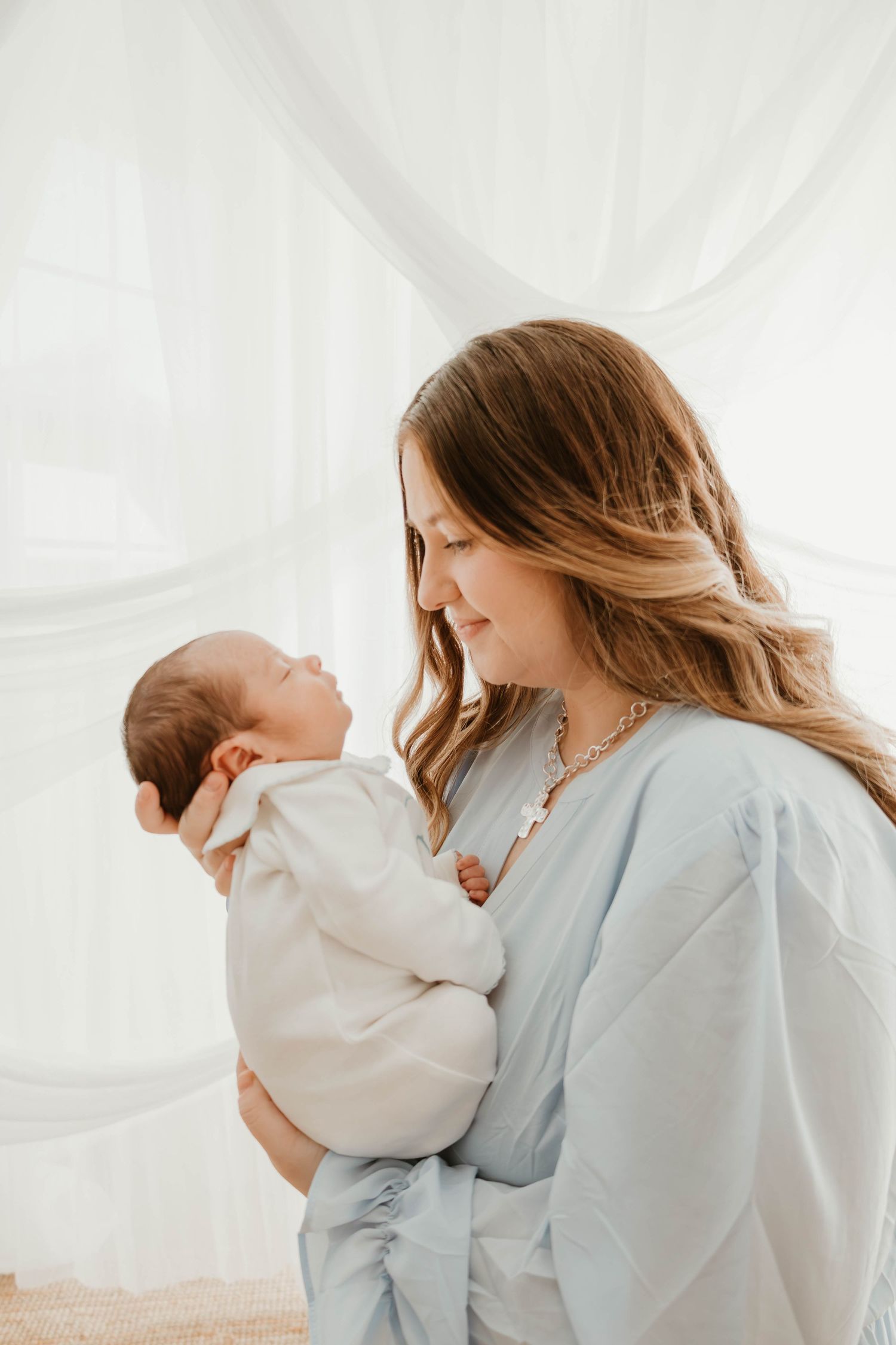 A tender moment between parent and child in white clothing against a light background with flowing fabric.