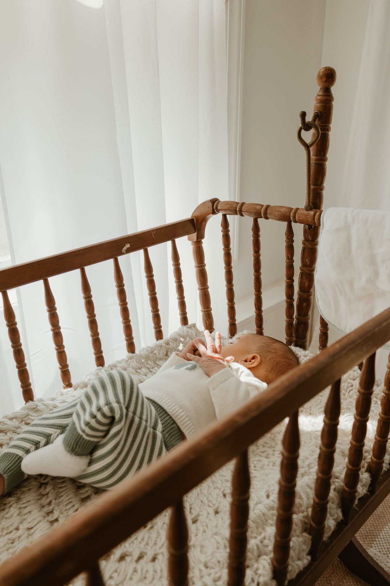 A wooden crib with a sleeping infant wrapped in a striped blanket resting inside.