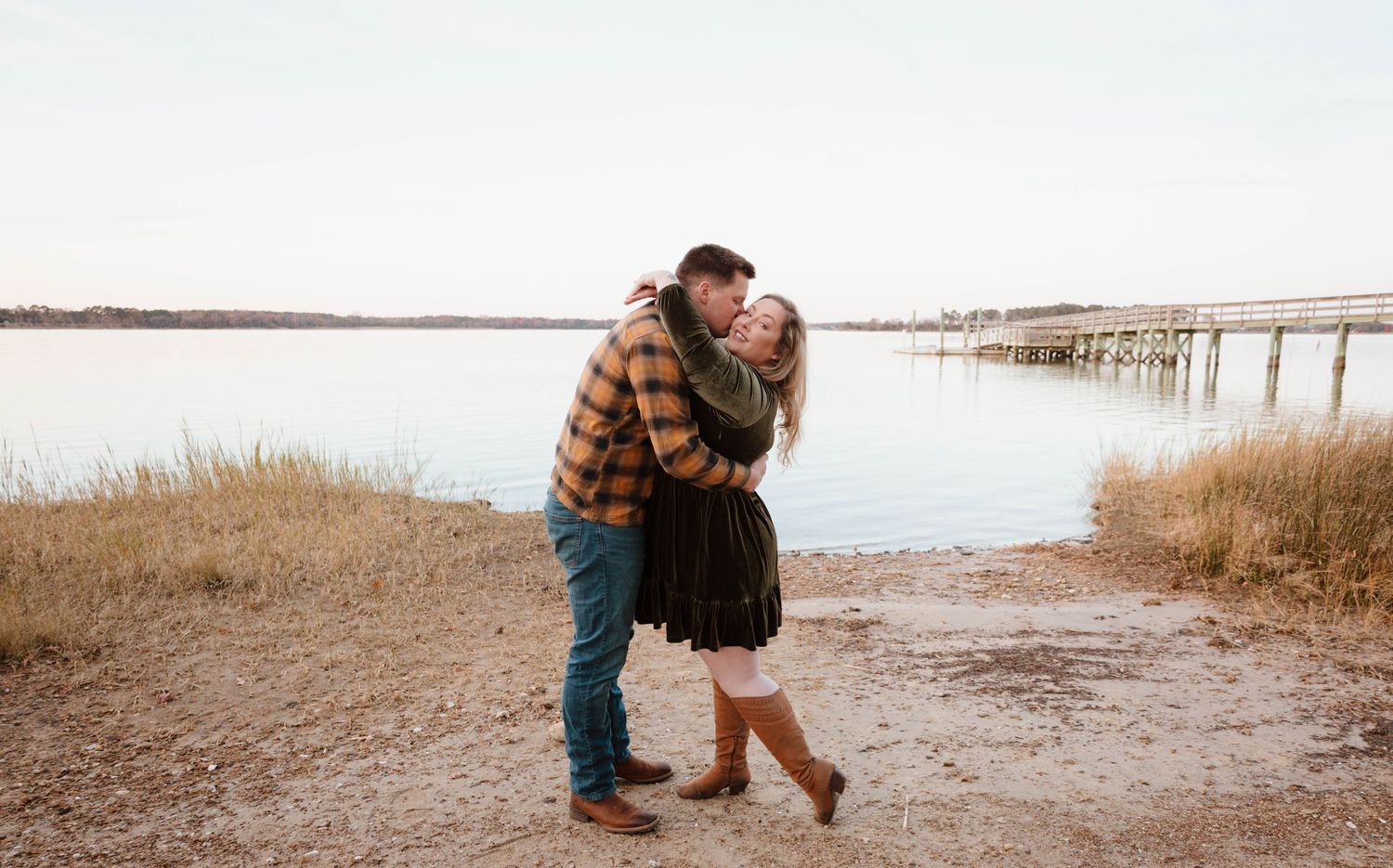 Couple sharing romantic moments on a lakeside beach at sunset.