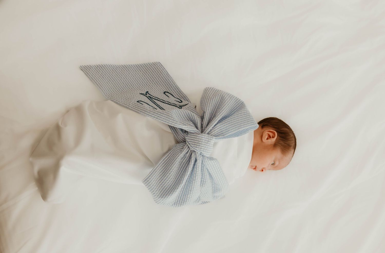 A sleeping baby swaddled in soft gray fabric lies peacefully on white bedding.