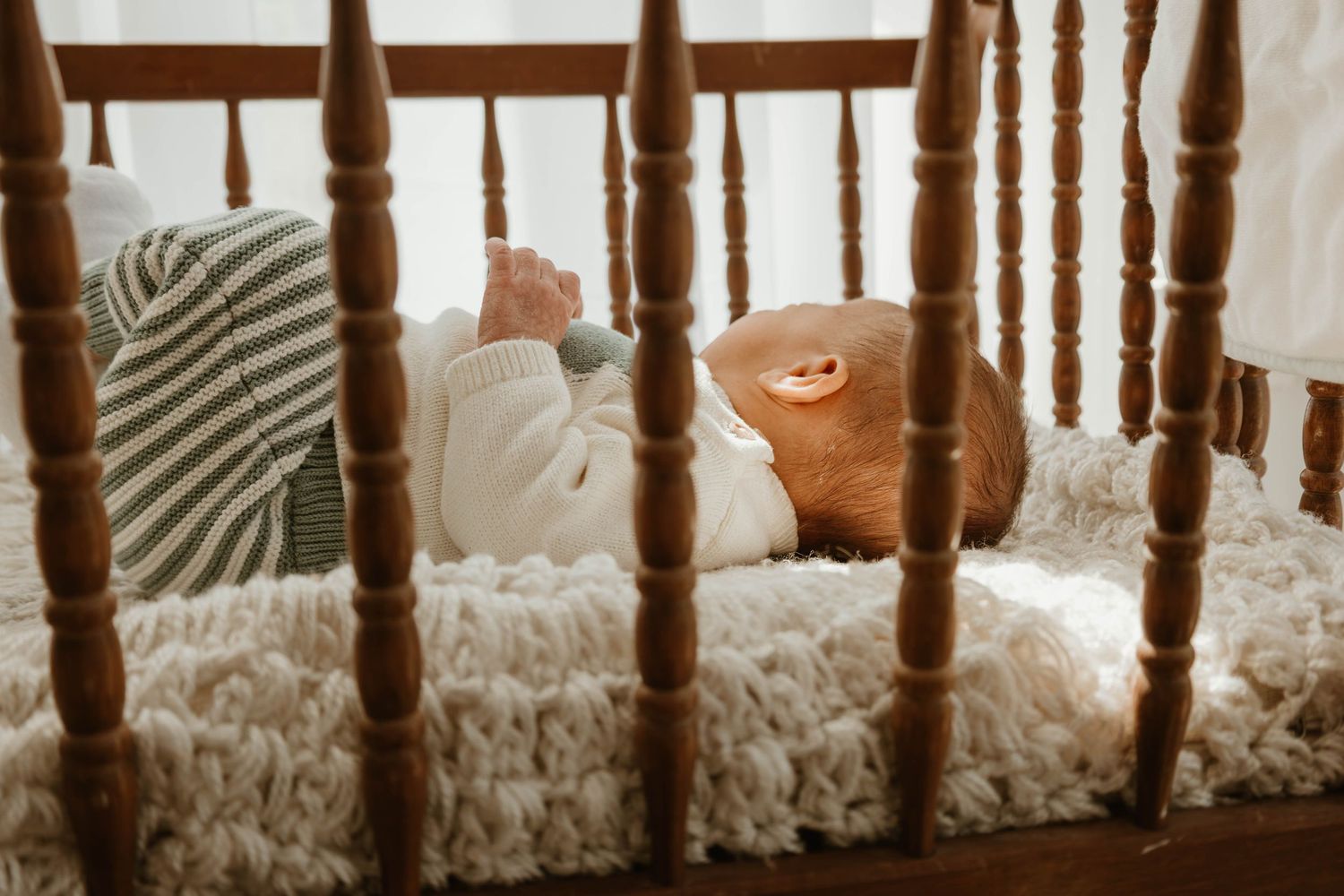 A wooden crib with a sleeping infant wrapped in a striped blanket resting inside.