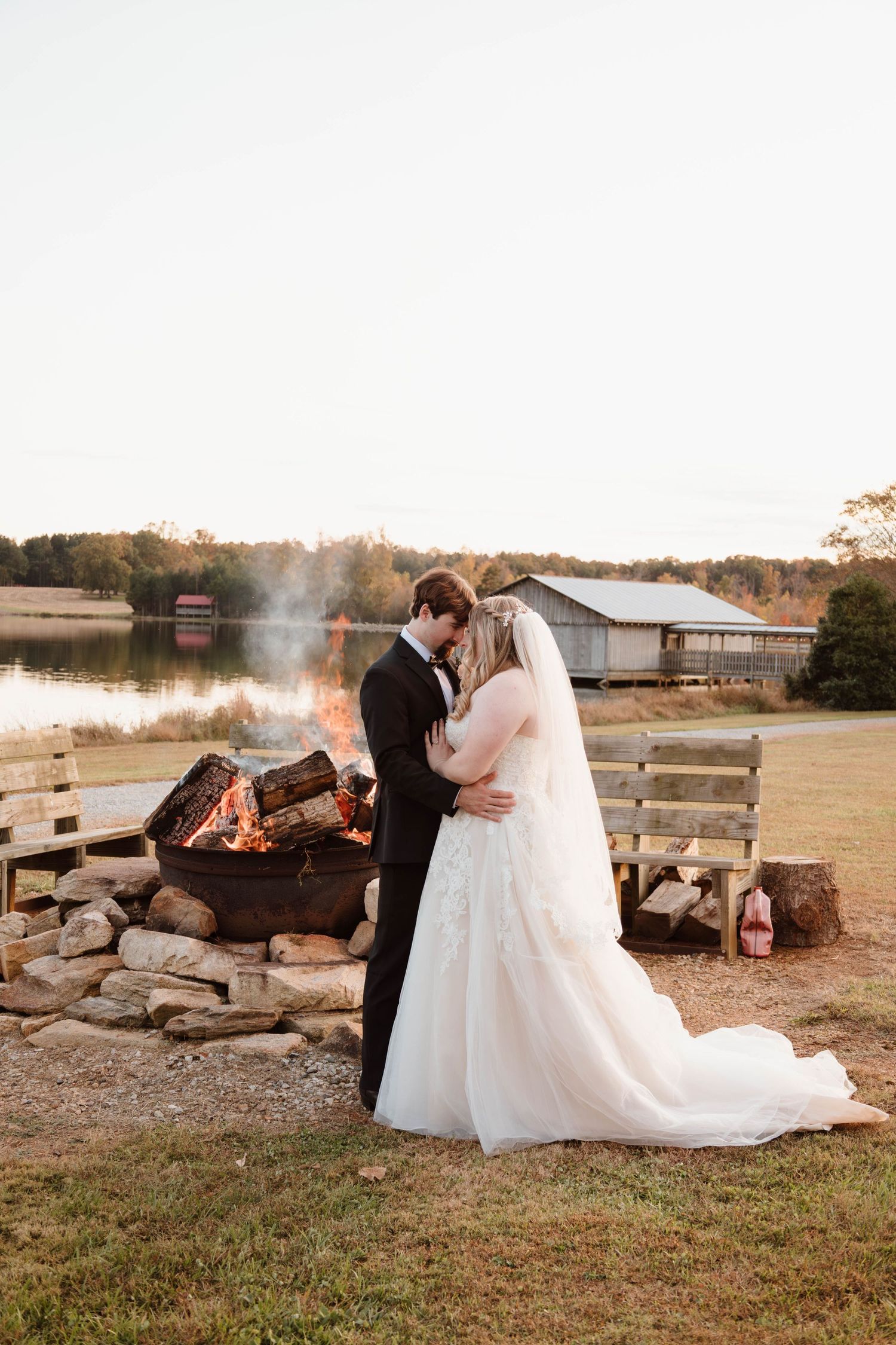 Newlyweds share an intimate moment by a rustic stone fire pit at dusk.