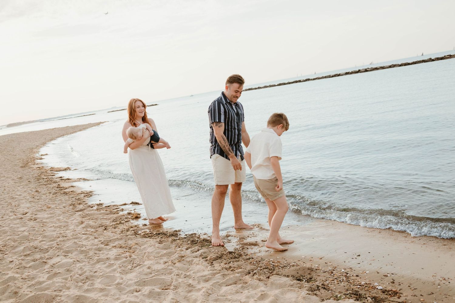 Family of three enjoying a sunny beach walk along the shoreline, with waves gently lapping at their feet.