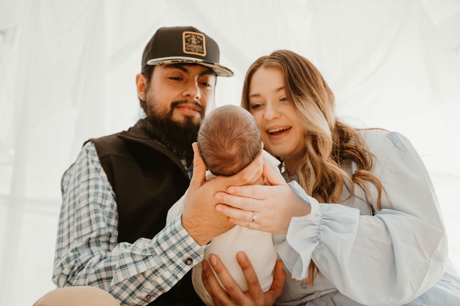 Family in casual attire sharing intimate moment with newborn baby against white background.