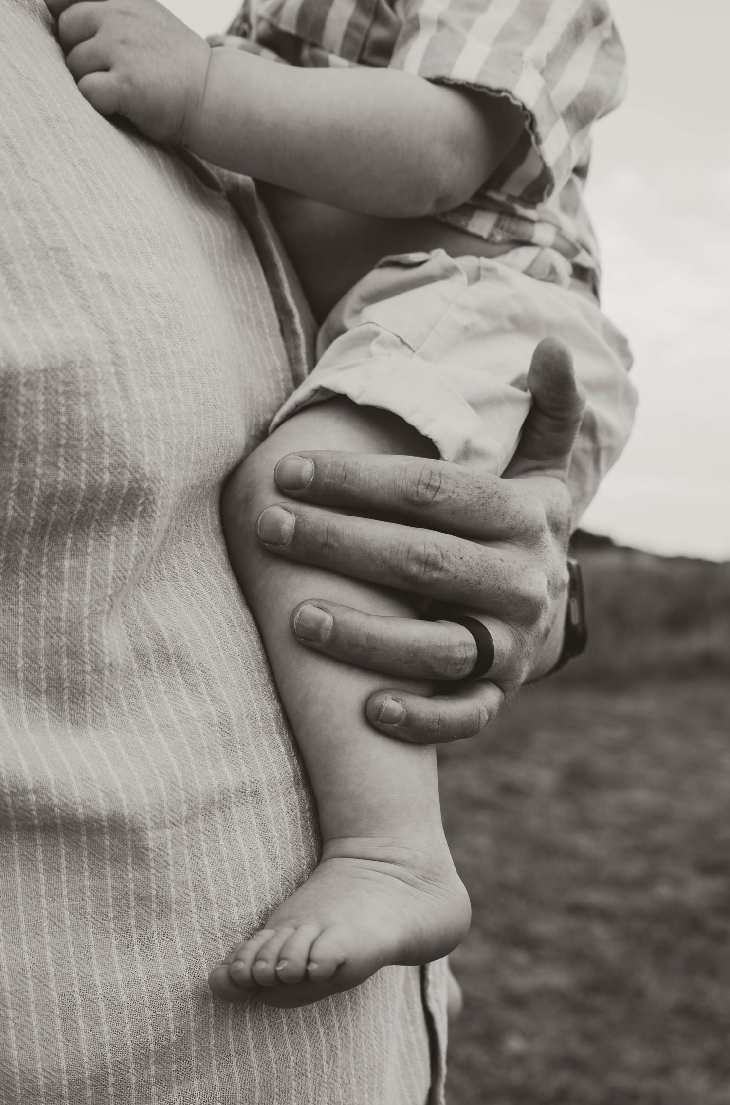 Black and white photo of an adult holding a baby, showing close-up of tiny feet and large hand.