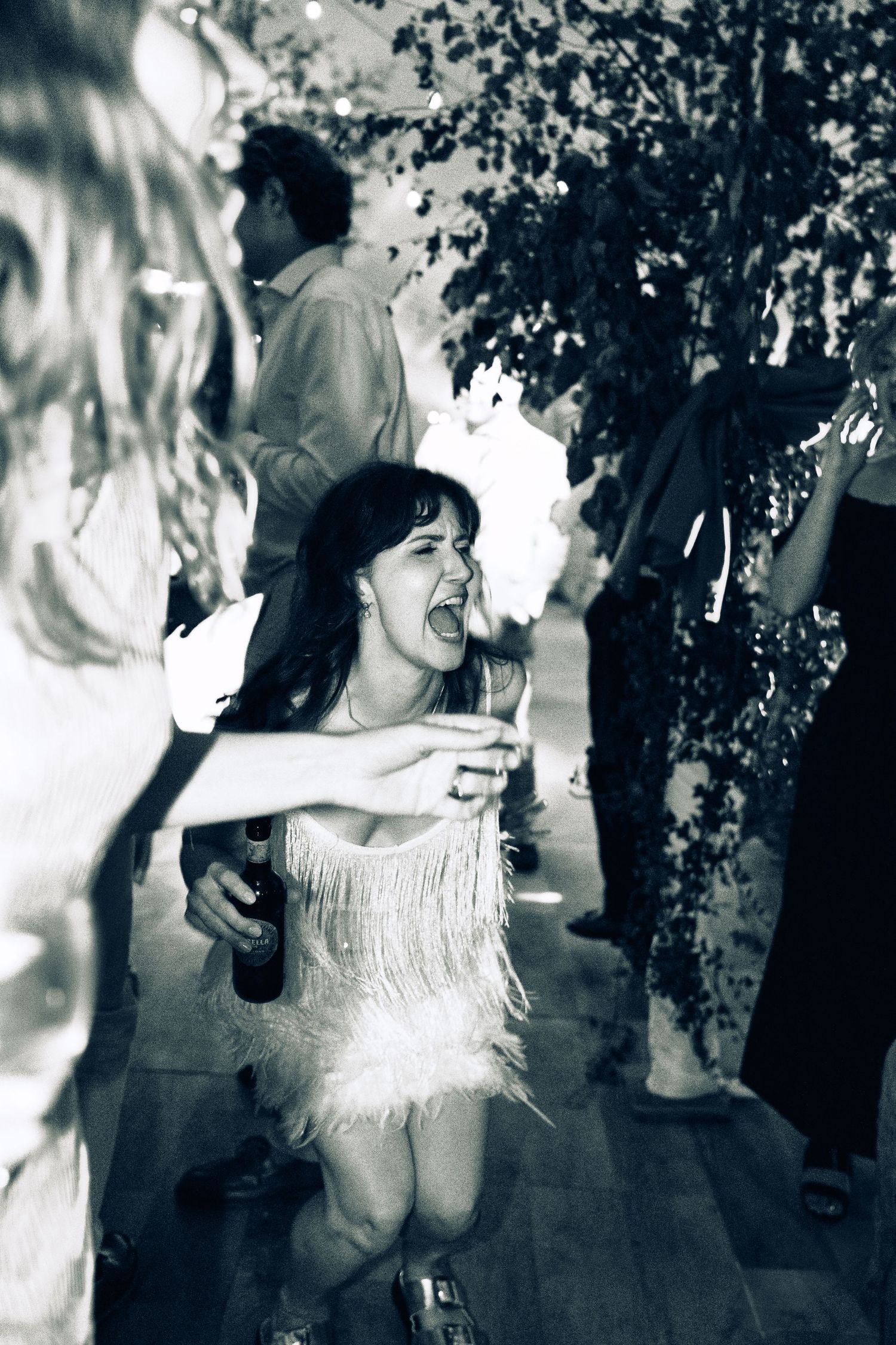 Black and white photo of a woman in a fringed dress dancing and laughing at a party.