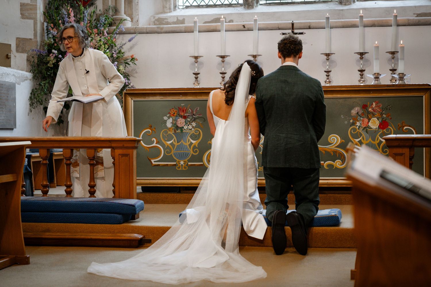 Bride and groom kneeling at church altar during wedding ceremony with officiant.