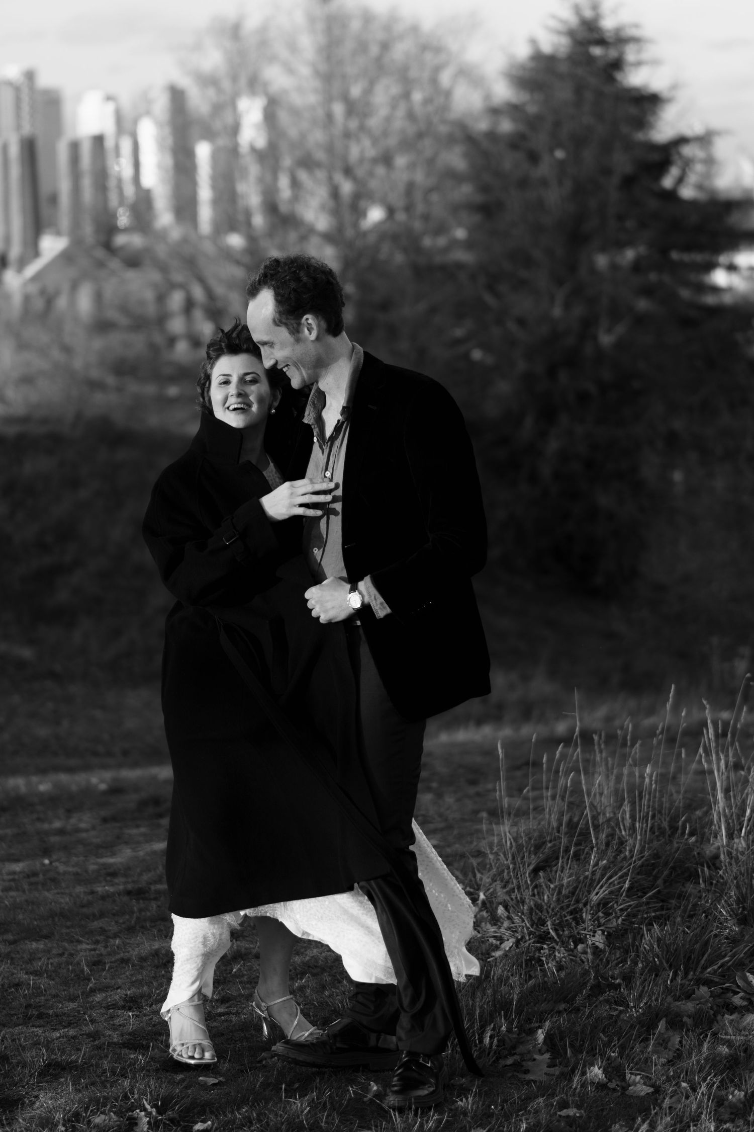 A romantic black and white photo of a couple embracing on a hilltop with a city skyline in the background.