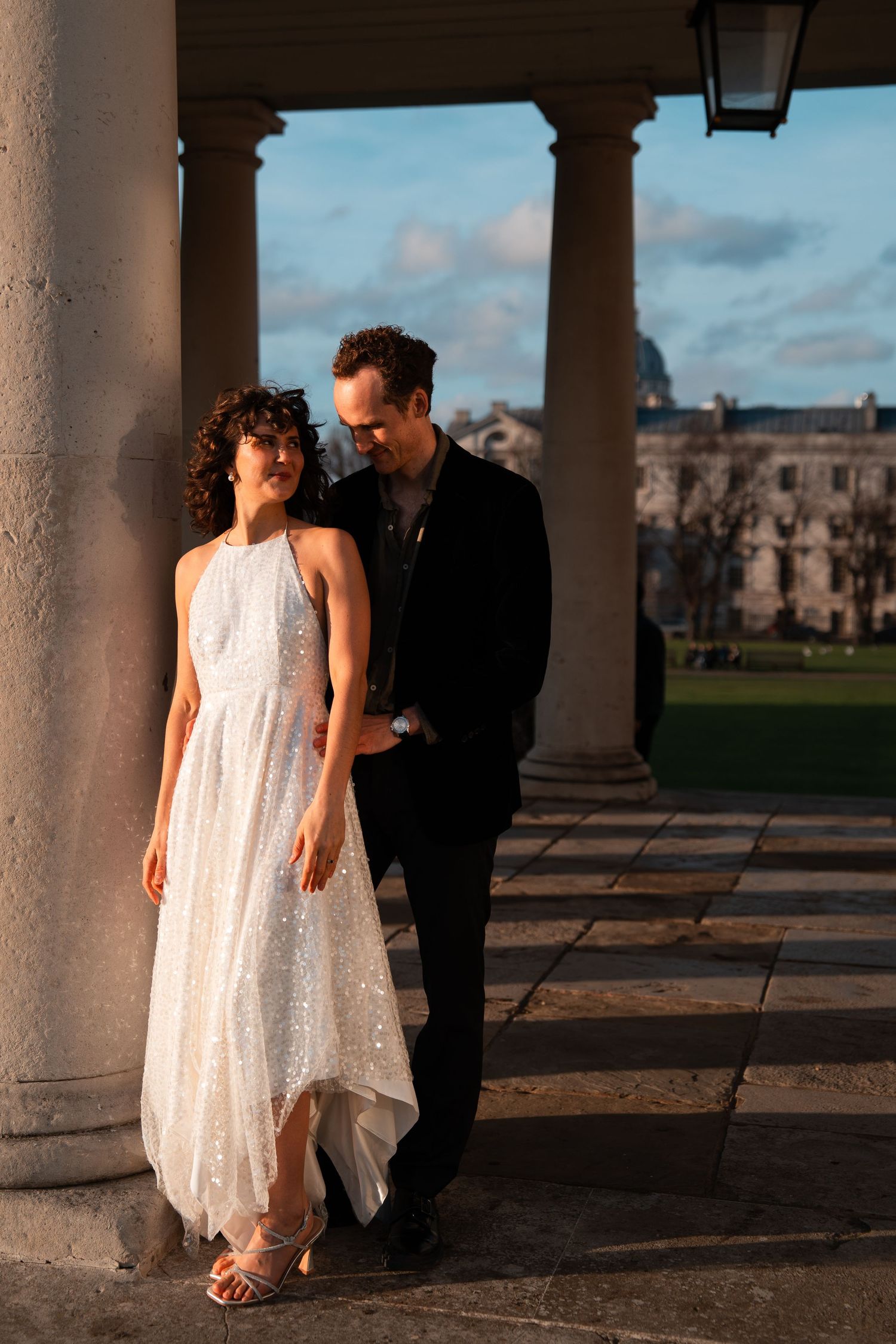 A flowing white dress catches the light as a couple shares a moment between classical columns.