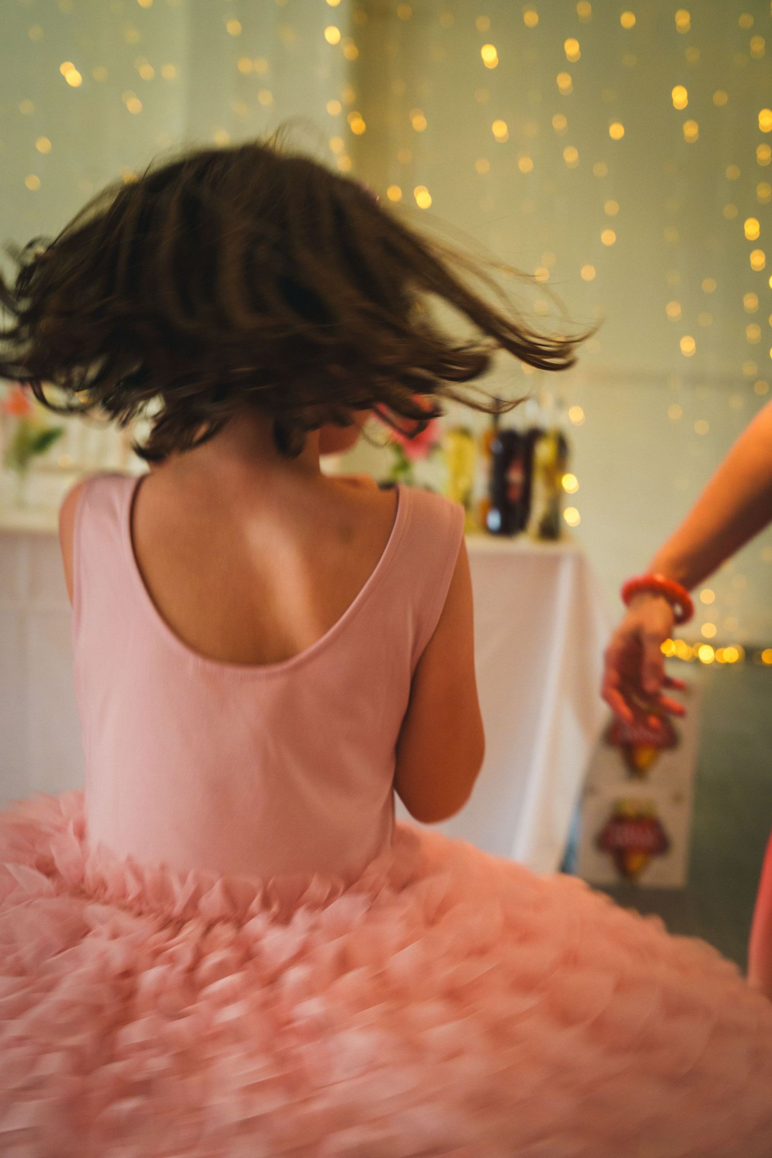 Young girl in pink tutu dress twirling at a party with bokeh fairy lights in the background.
