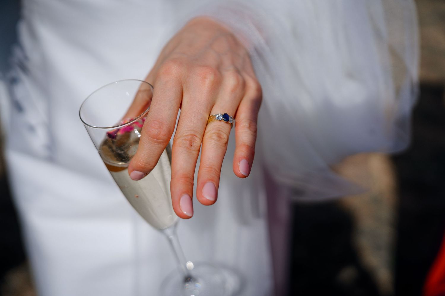 Close-up of bride's hand holding champagne flute displaying elegant sapphire engagement ring.