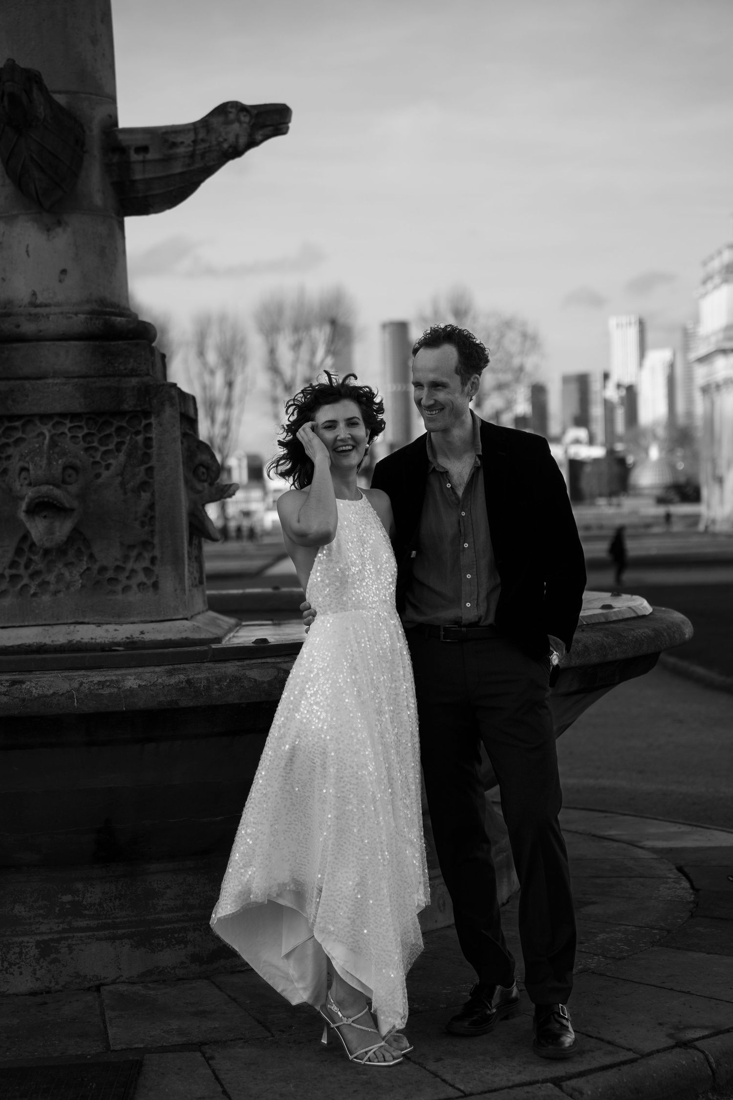 A couple in formal attire poses against stone pillars in black and white.