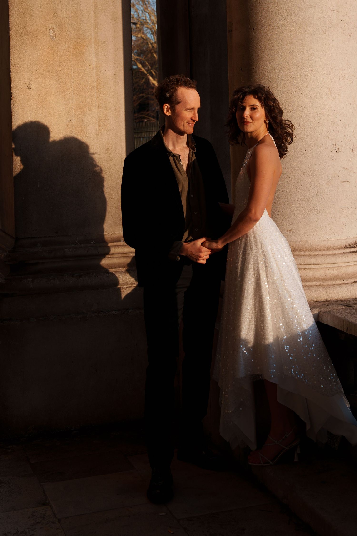 Dramatic lighting illuminates a couple's intimate moment between classical stone columns.