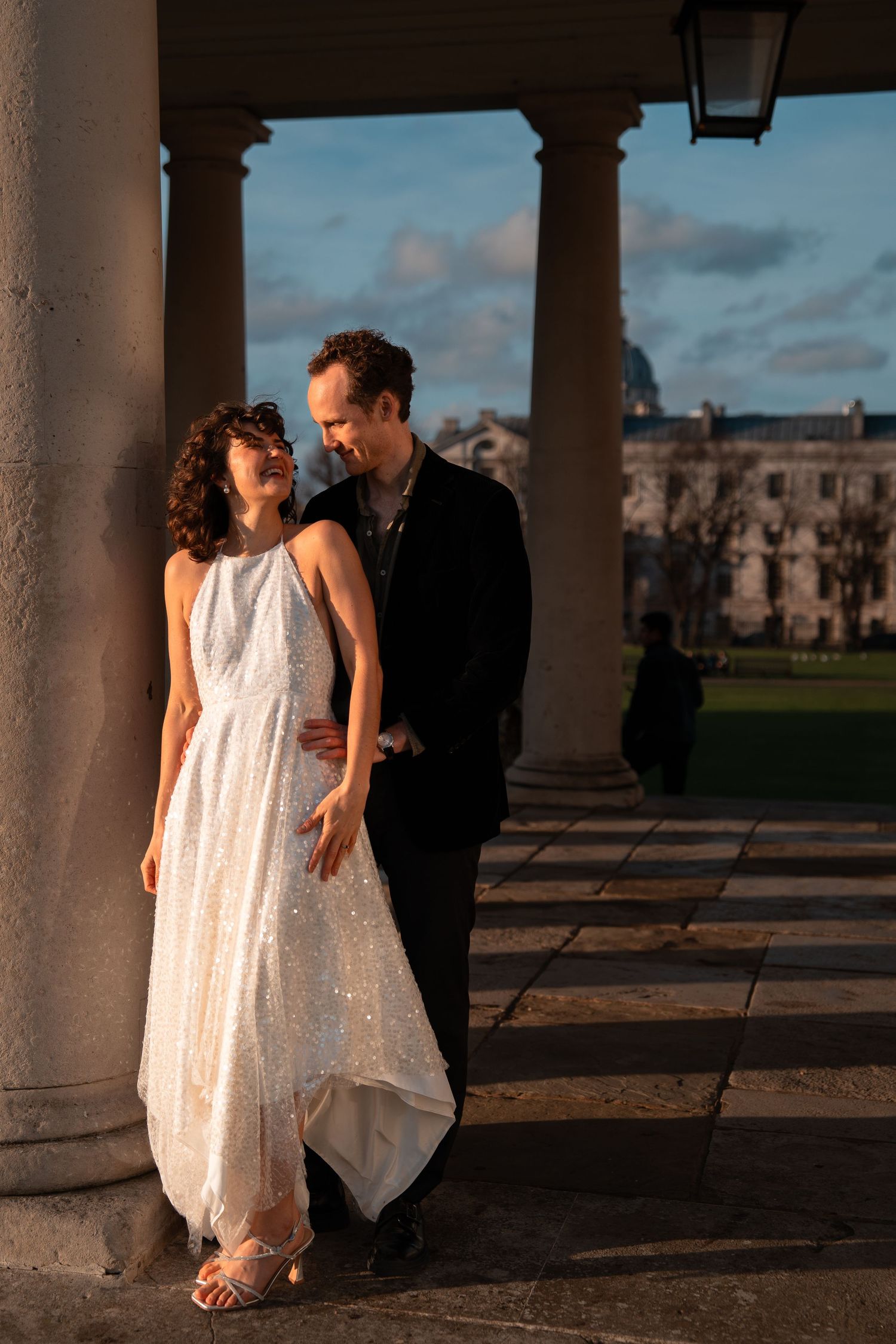 Two people share a playful moment under an ornate colonnade during sunset.