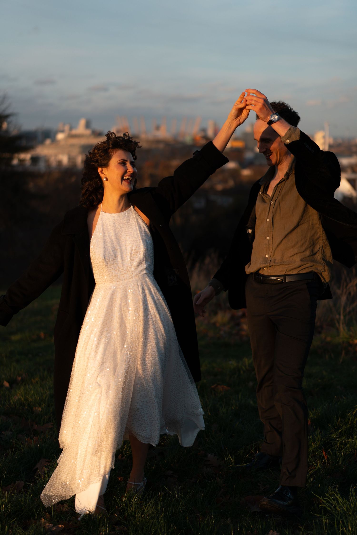 Dancers move energetically on a hilltop with dramatic sunset lighting and city views.