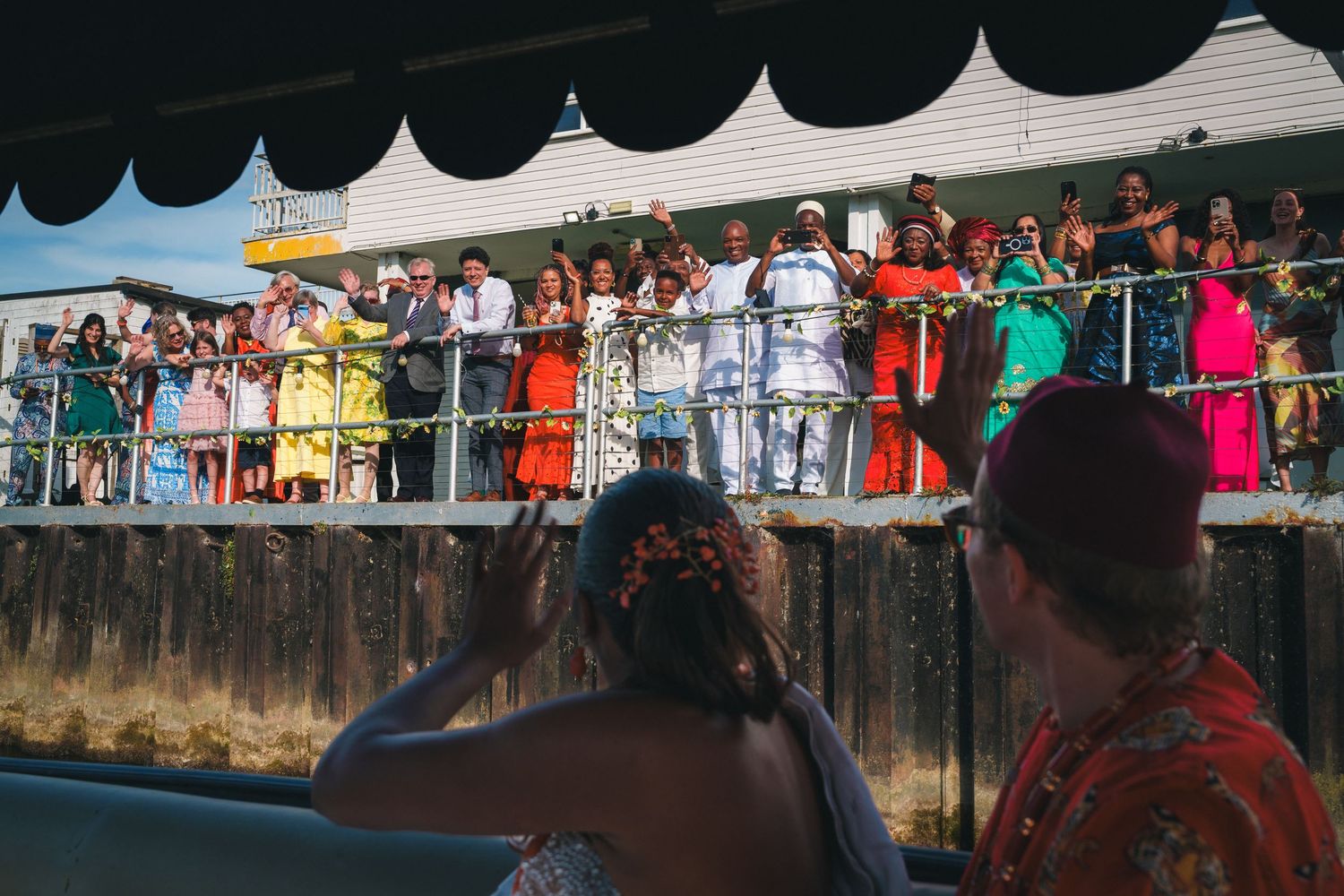 Colorful crowd gathered on a decorated balcony watching a festive outdoor celebration or parade below.
