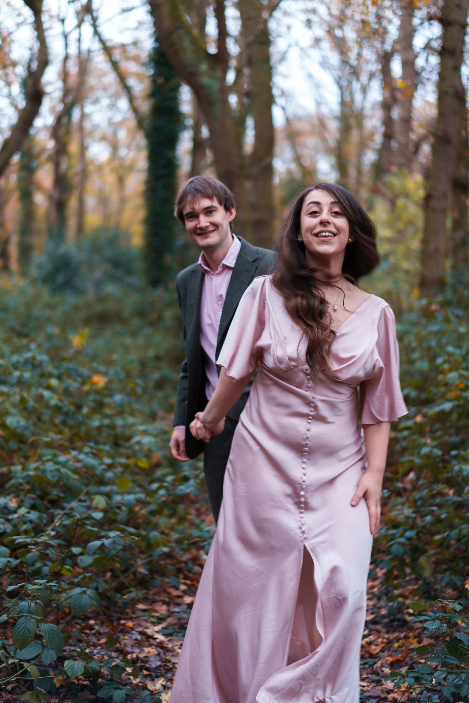 A couple walking through an autumn forest, with the woman wearing a flowing pink dress.
