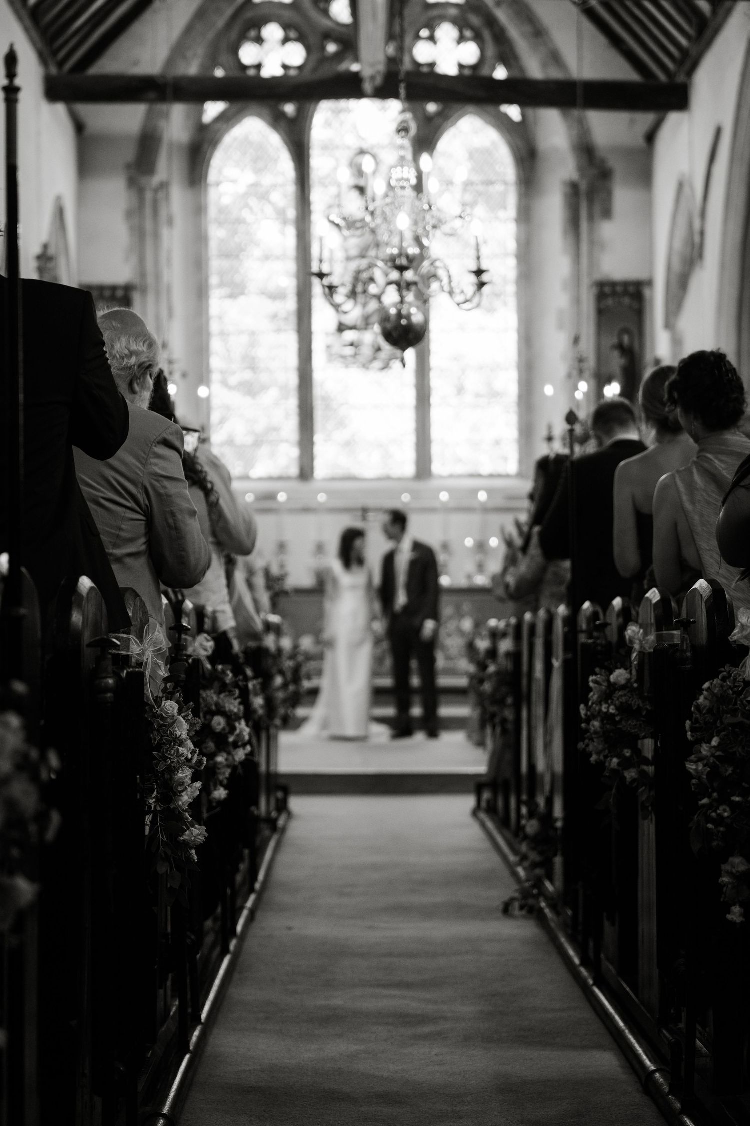 Black and white photo of wedding ceremony in historic church with guests in pews.