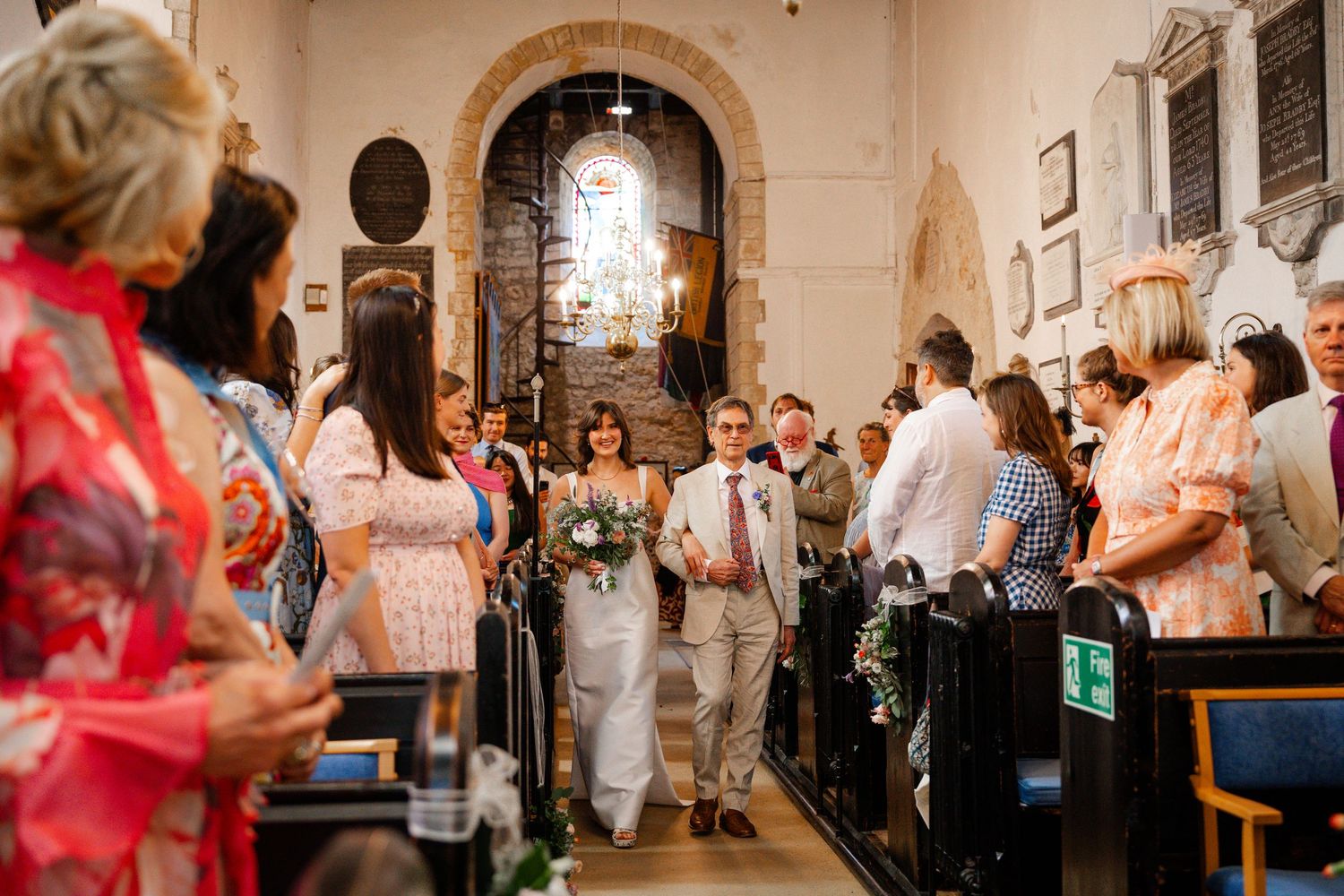 Bride and groom walking down the aisle of a historic stone church surrounded by wedding guests.