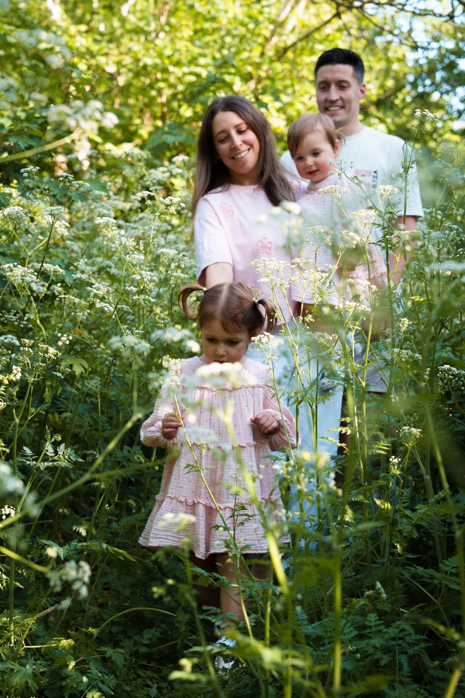 Happy family with two young daughters walking through lush green wildflower meadow on a sunny day.