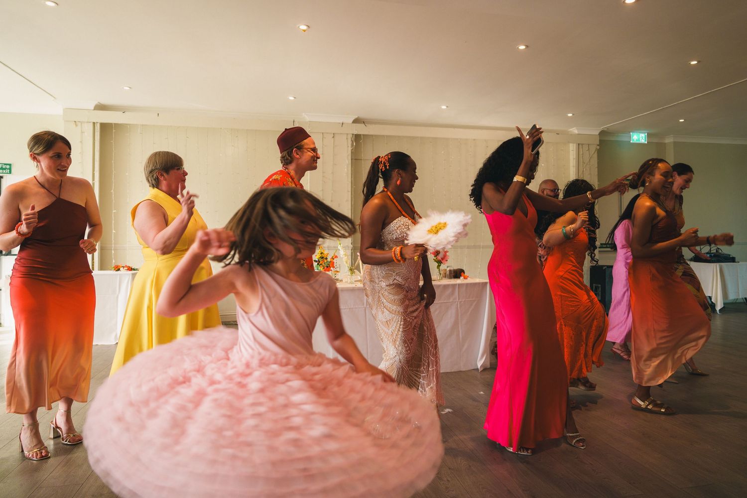 Colorful wedding reception dance floor with bridesmaids in vibrant dresses dancing joyfully at an elegant indoor venue.