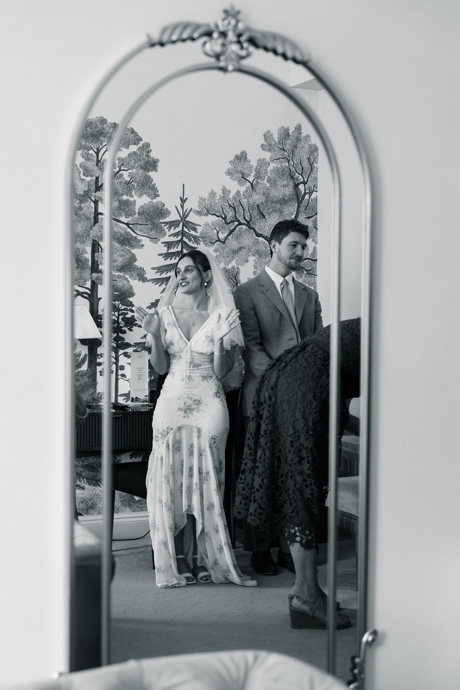 Black and white mirror reflection of bride in lace gown and groom in suit at elegant wedding venue.