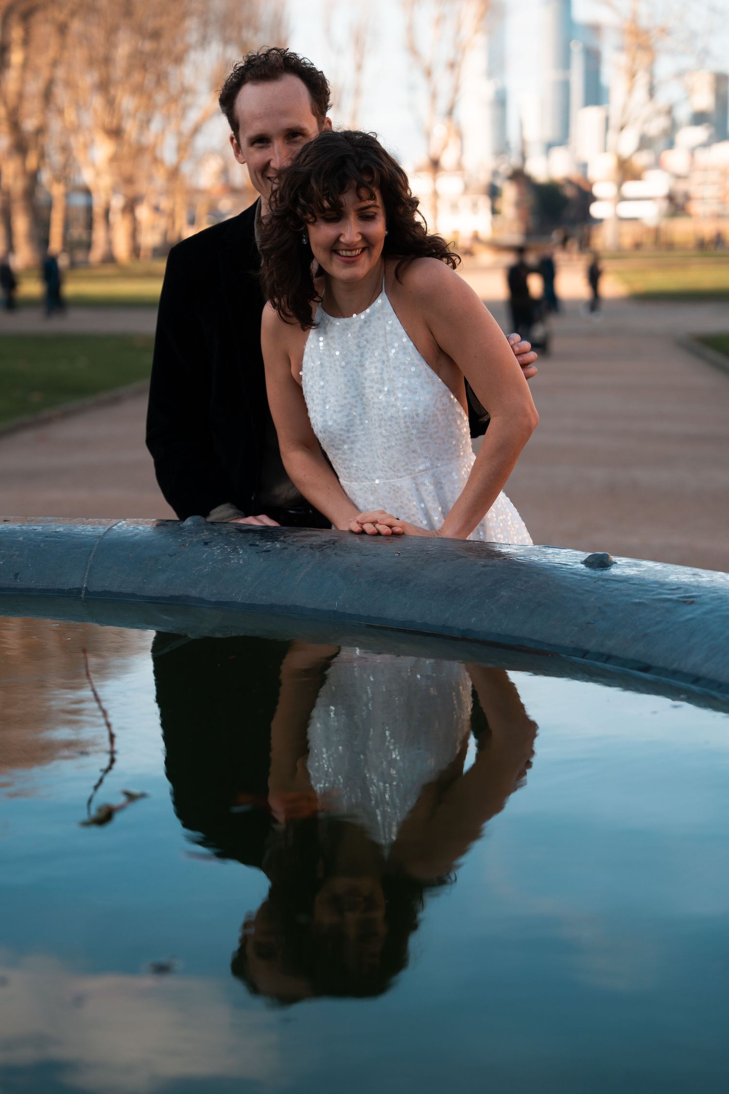 A couple leans over to look at their reflection in a pool of water.