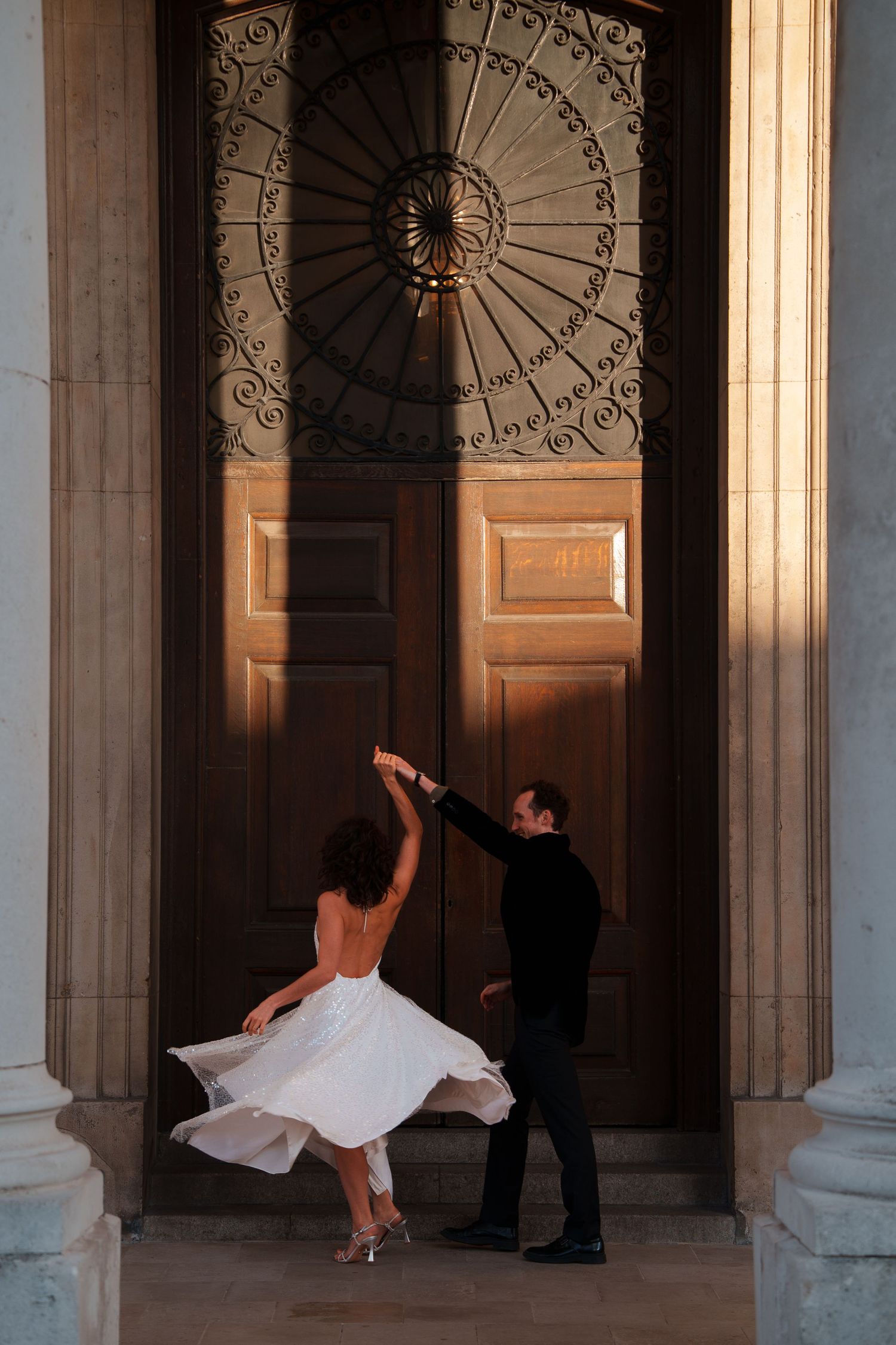 A couple dances gracefully between ornate stone pillars and wooden doors.