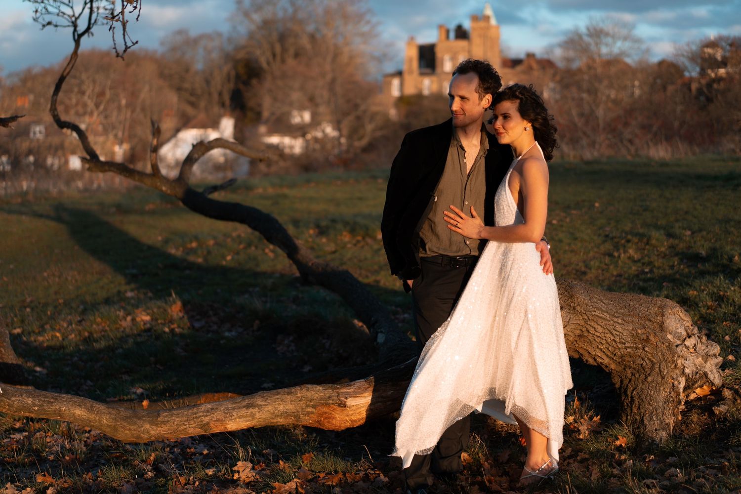 A couple embraces during a sunset photoshoot with urban and natural elements in the background.