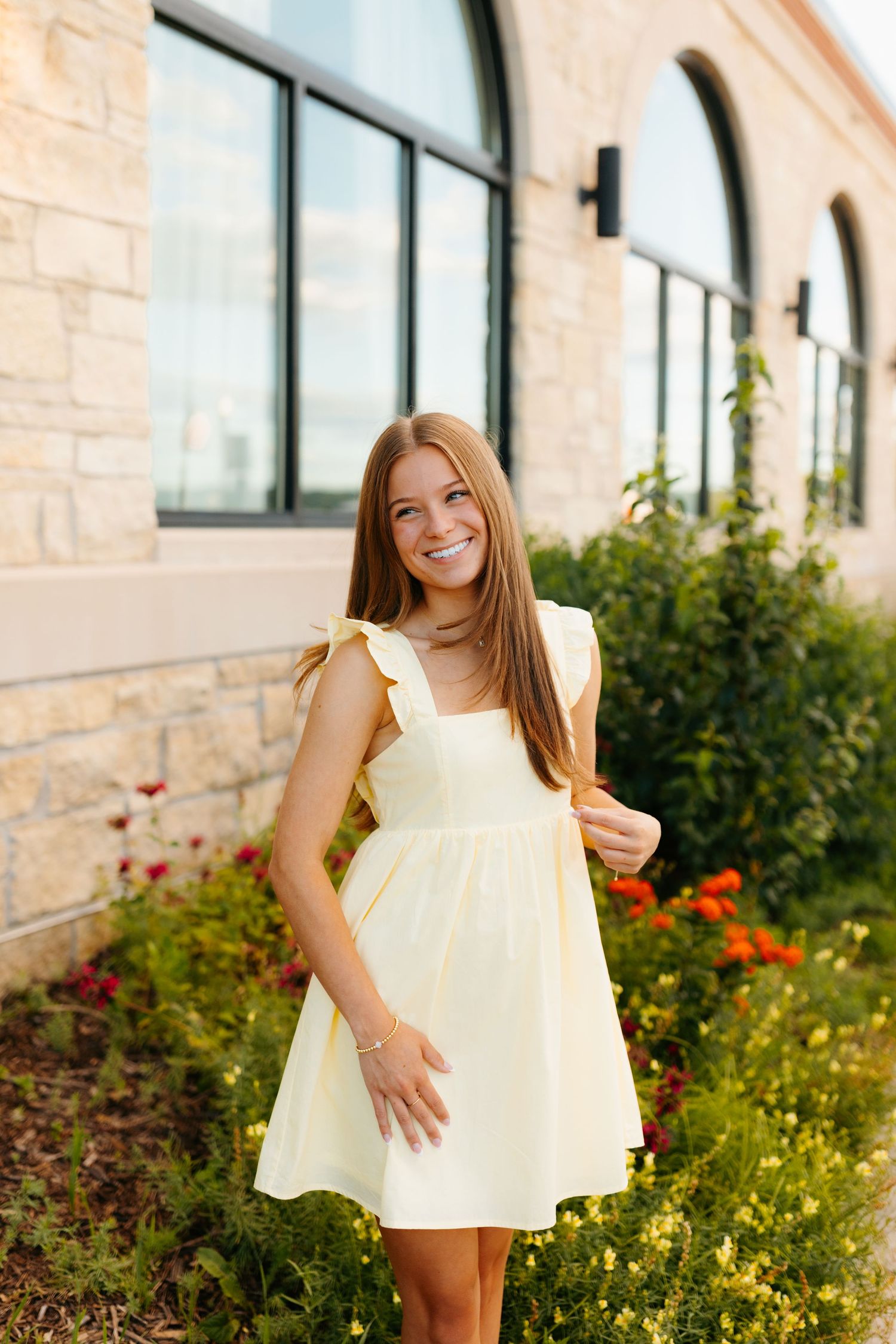Cream colored ruffle dress photographed near stone building with orange and yellow garden flowers.