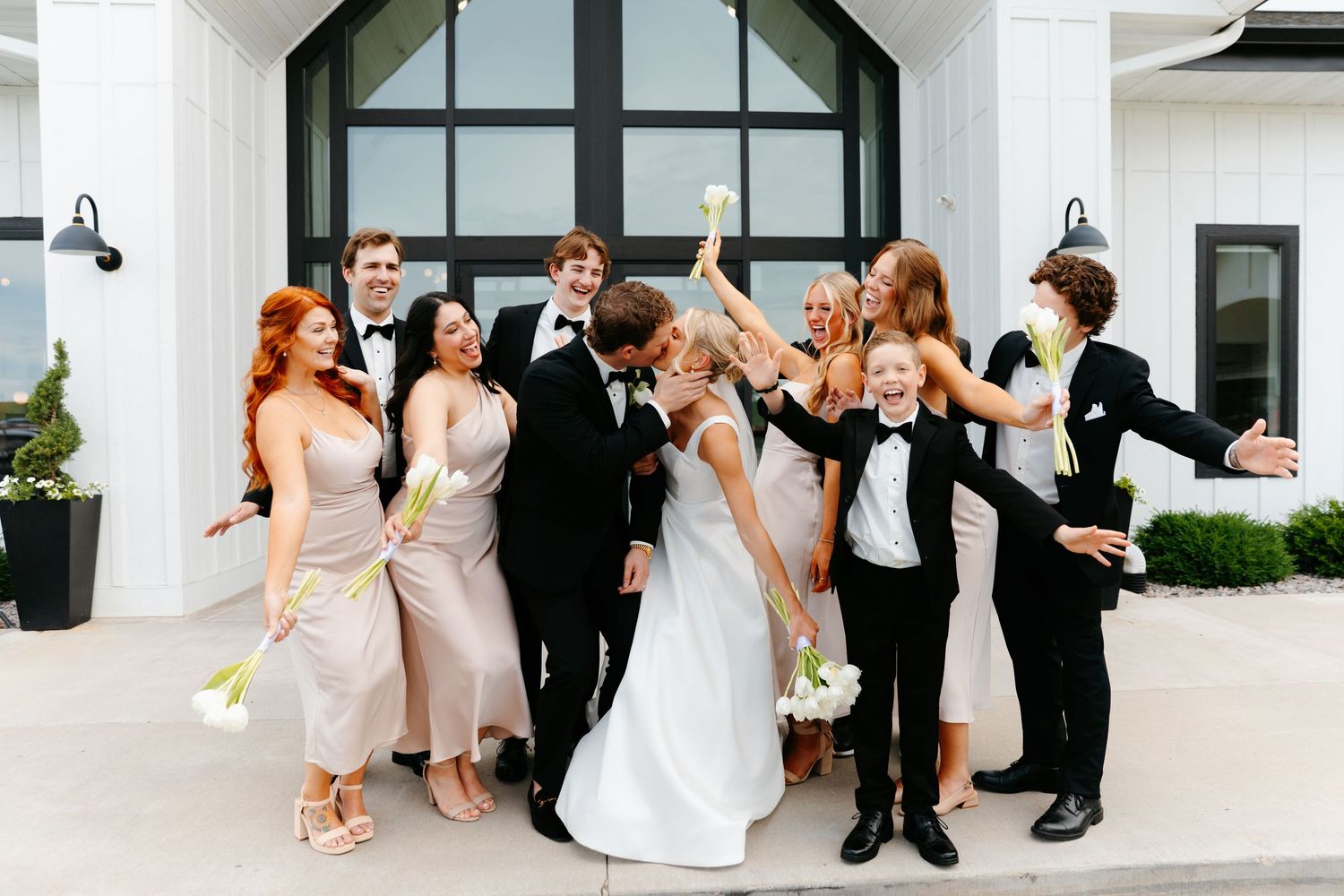 Wedding party having fun with candid poses outside white chapel.