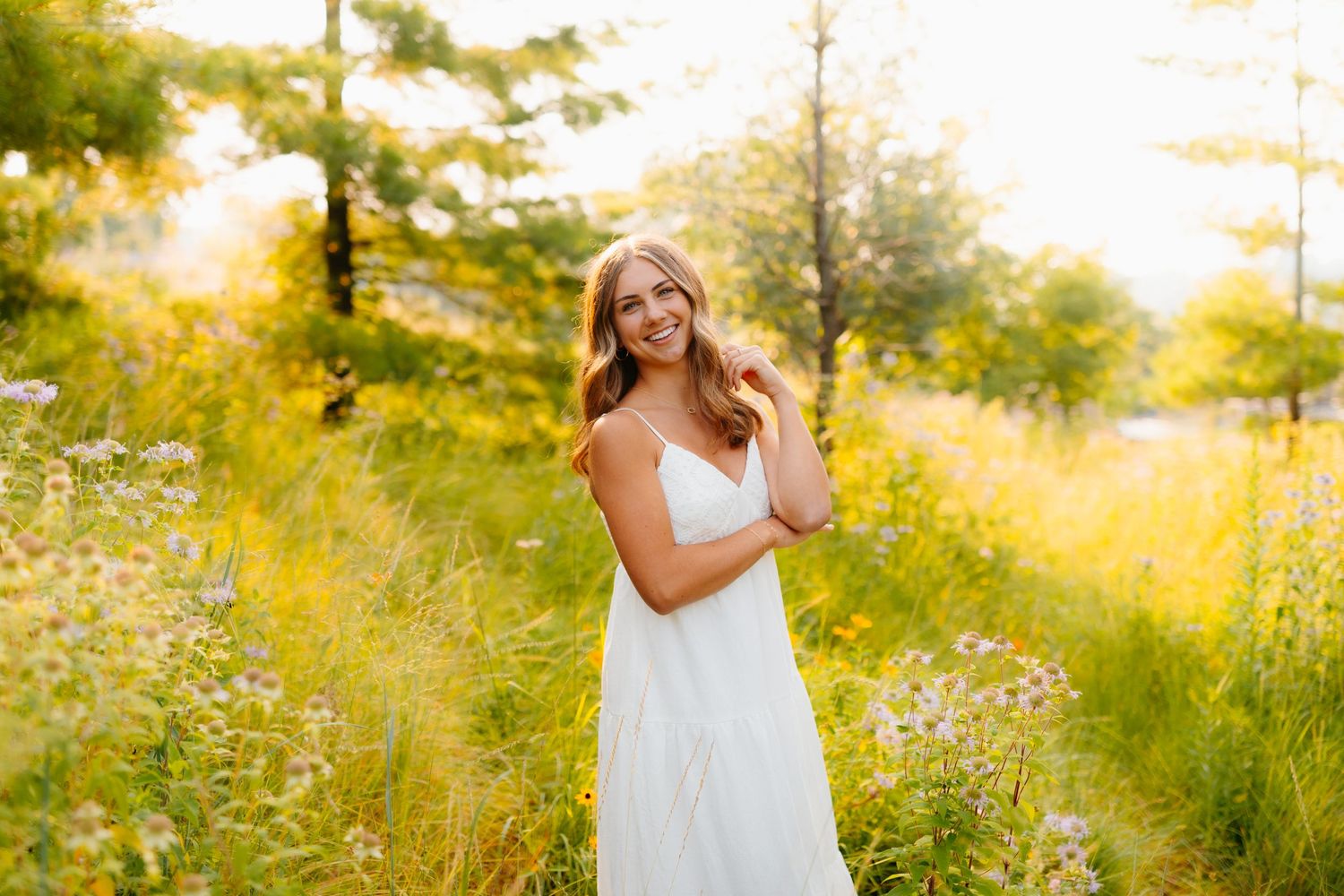 Flowing white dress captured in a sunlit meadow with wildflowers and tall grass.