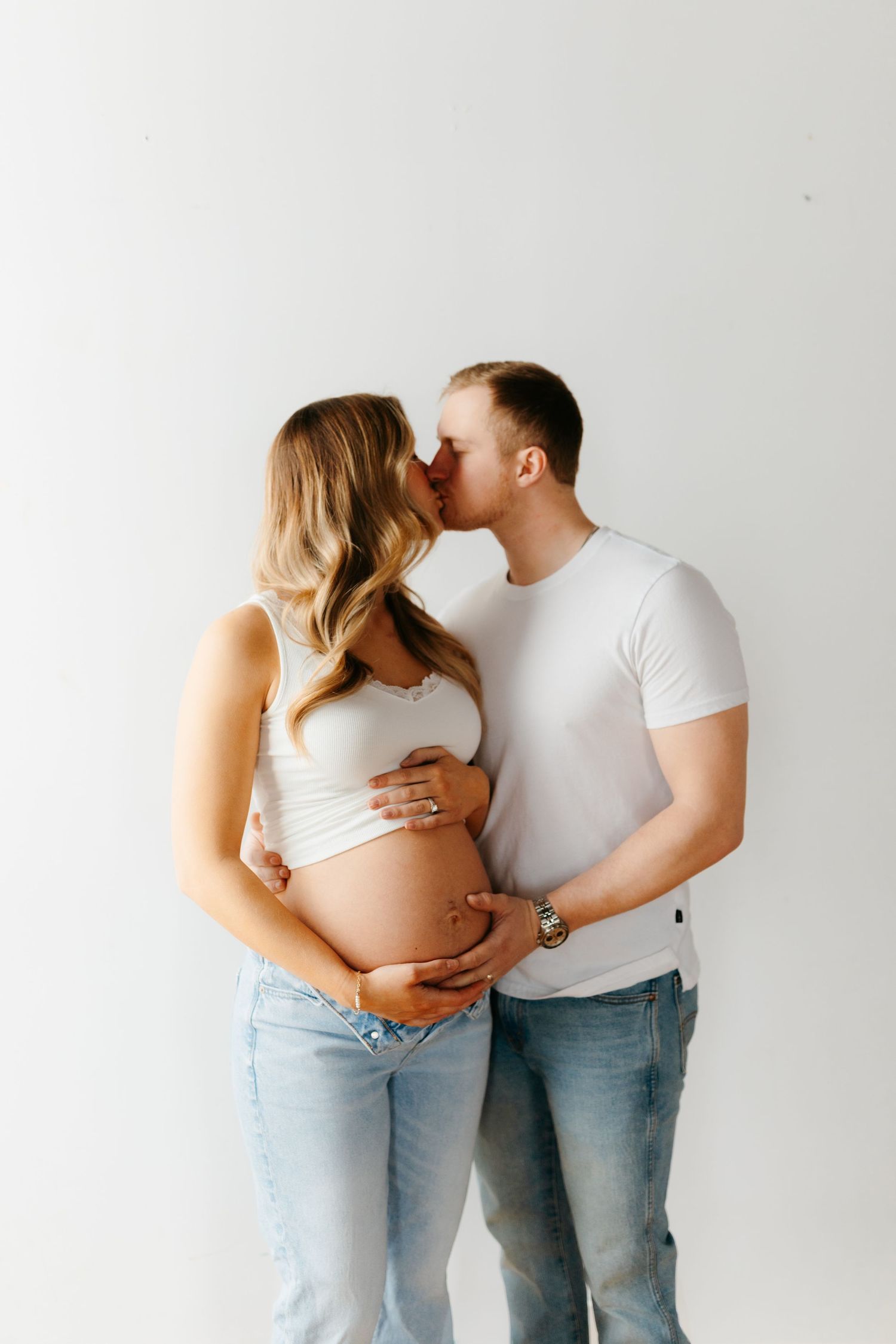 A couple in casual denim embraces against a white studio backdrop.