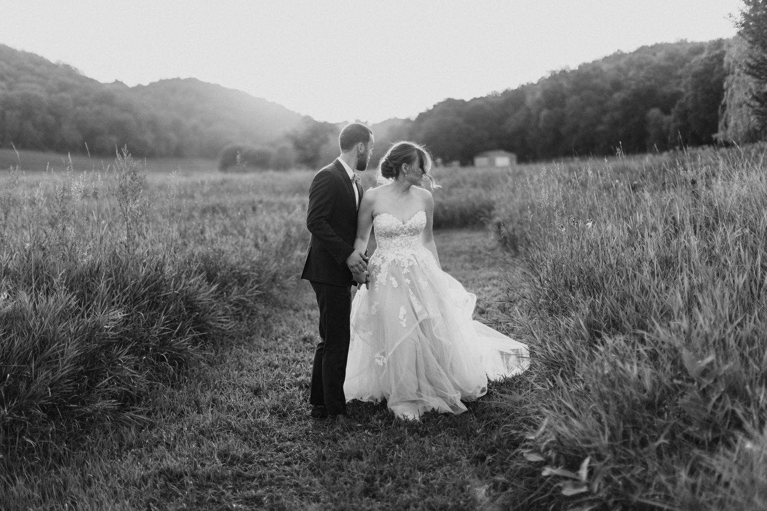 Newlyweds share an intimate moment in a rustic field during golden hour.