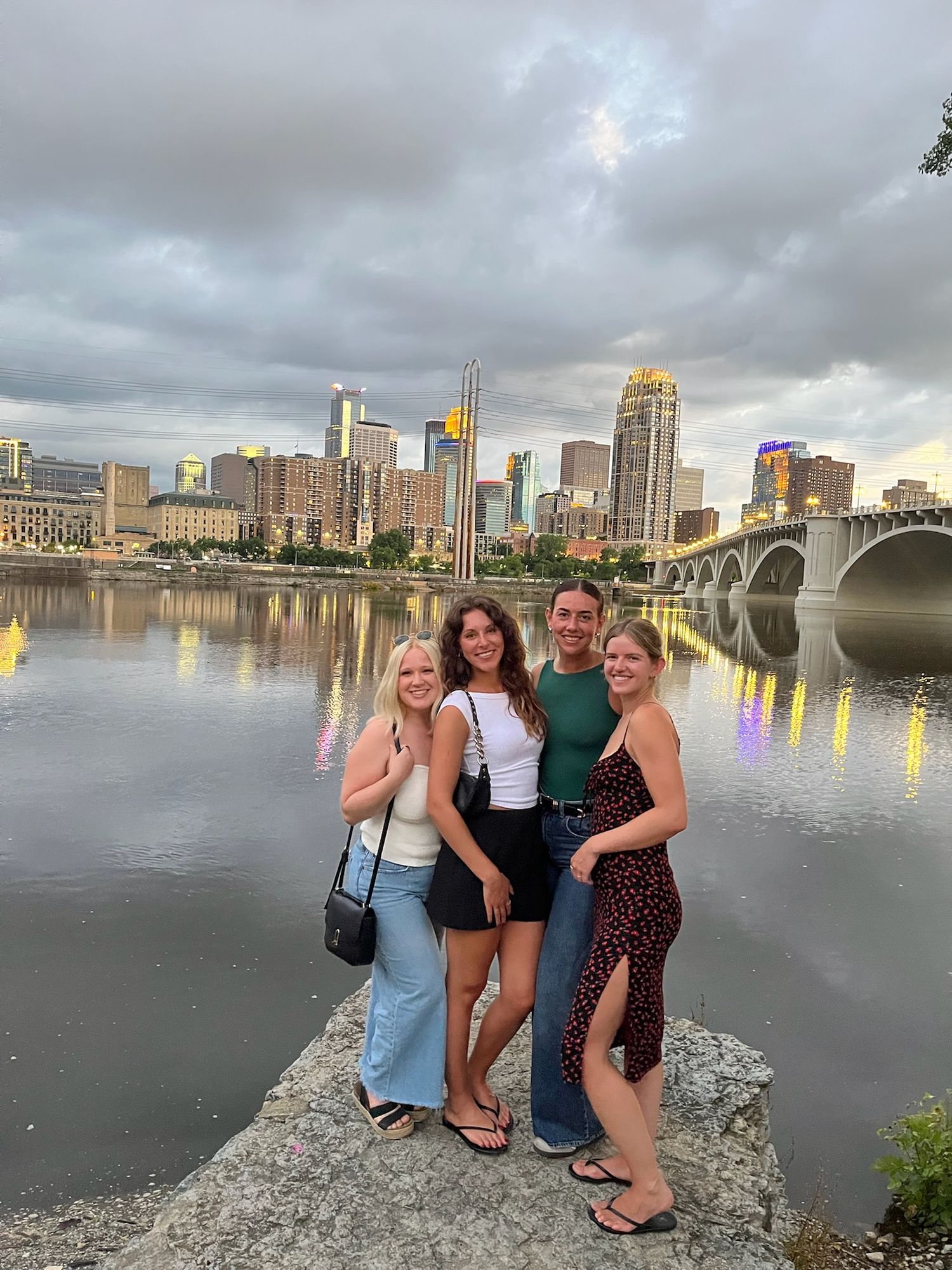 Friends pose together by Minneapolis skyline and Stone Arch Bridge at dusk.