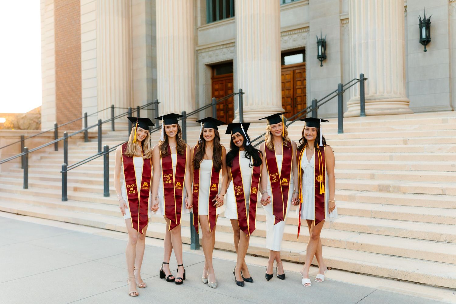 Group poses on grand white stone steps of classical building with columns.