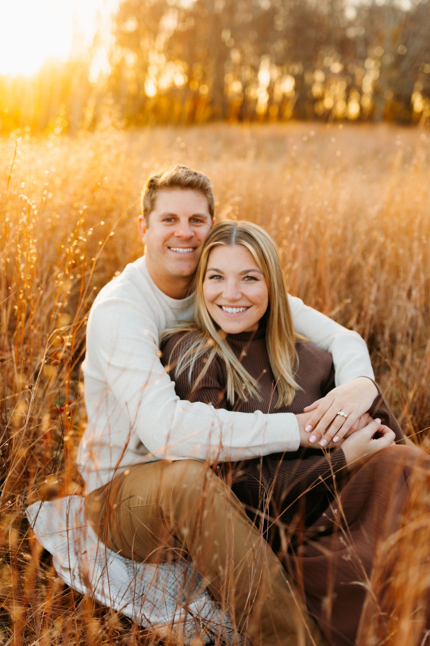 A couple shares a candid moment while sitting in a golden field at sunset.