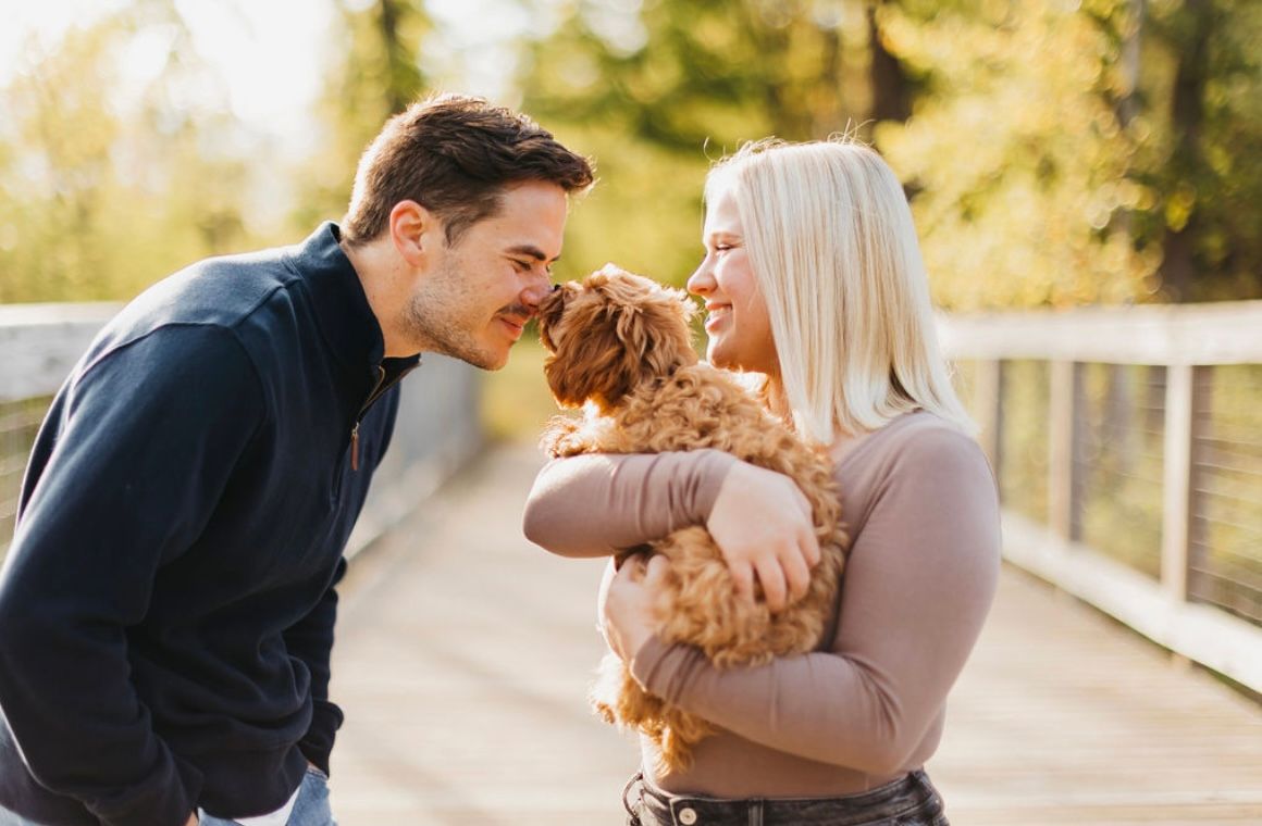 Happy couple plays with their fluffy goldendoodle puppy during outdoor photoshoot.