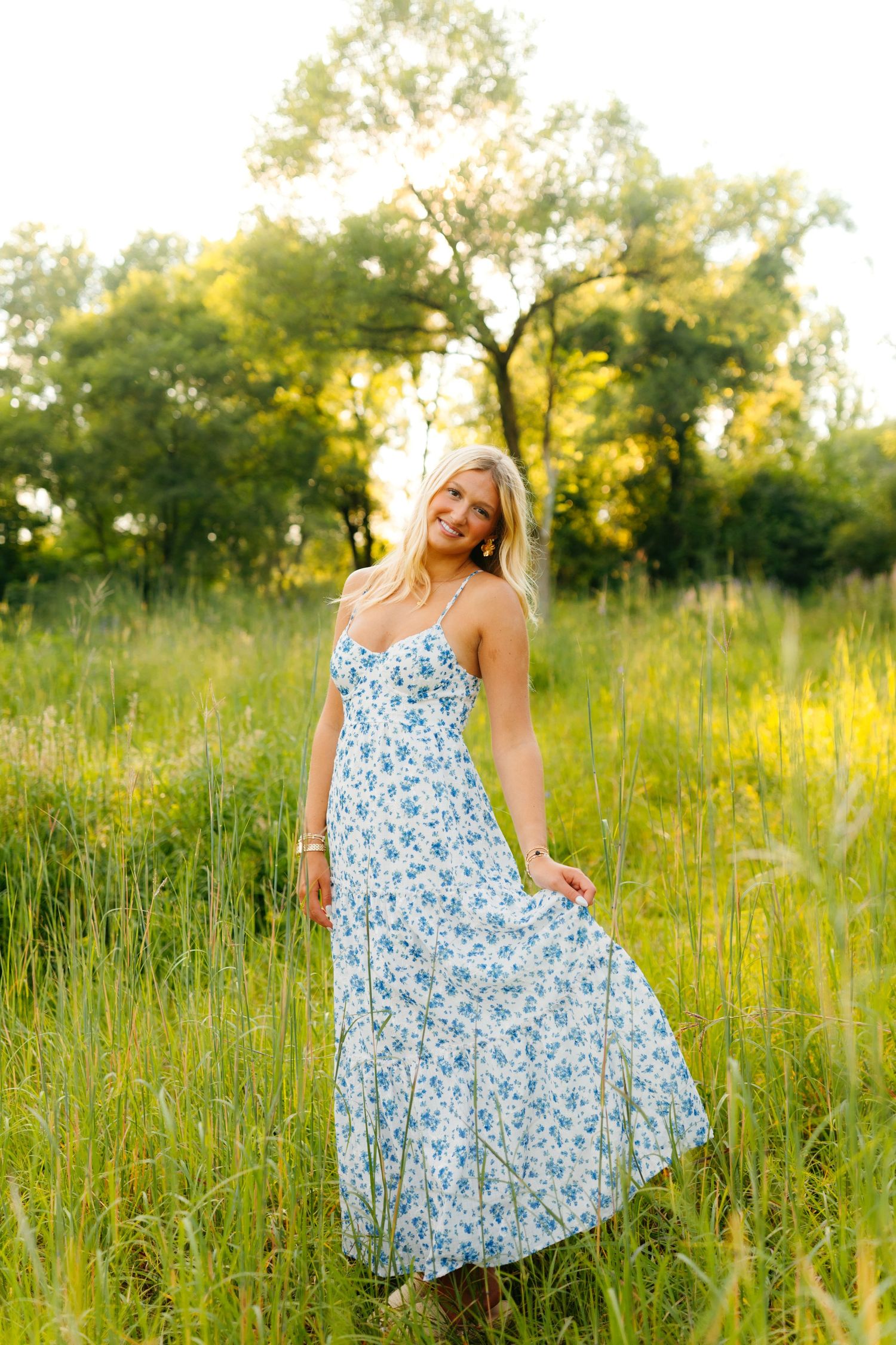 A woman in a floral maxi dress poses in a sunlit meadow with tall grass.