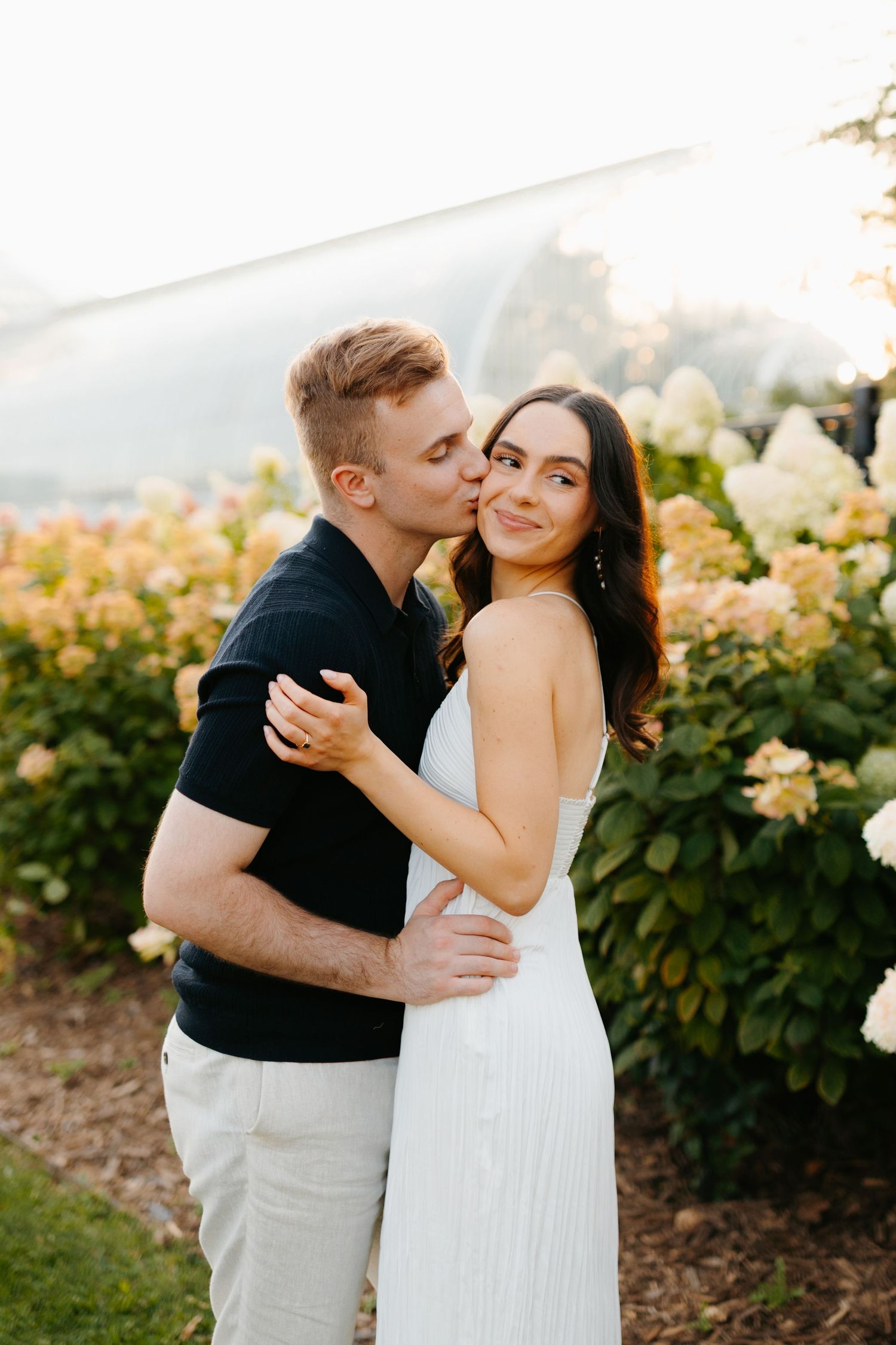 Couple sharing intimate moment against floral garden backdrop.
