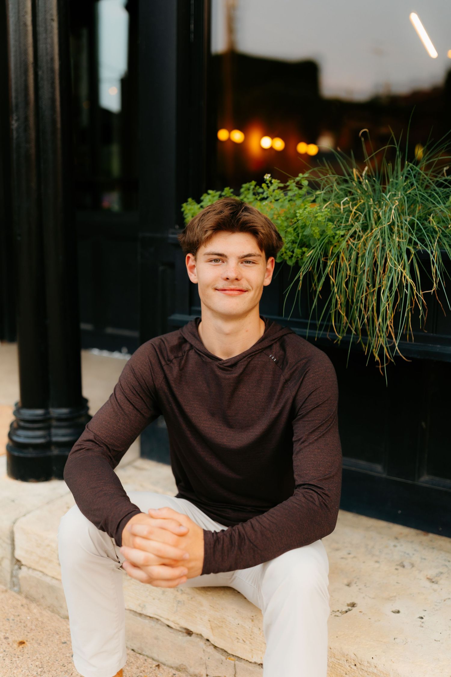Portrait against stone columns wearing dark sweater and light pants.