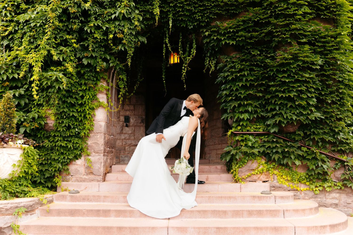 Wedding couple poses on ivy-covered stone steps in romantic garden setting.